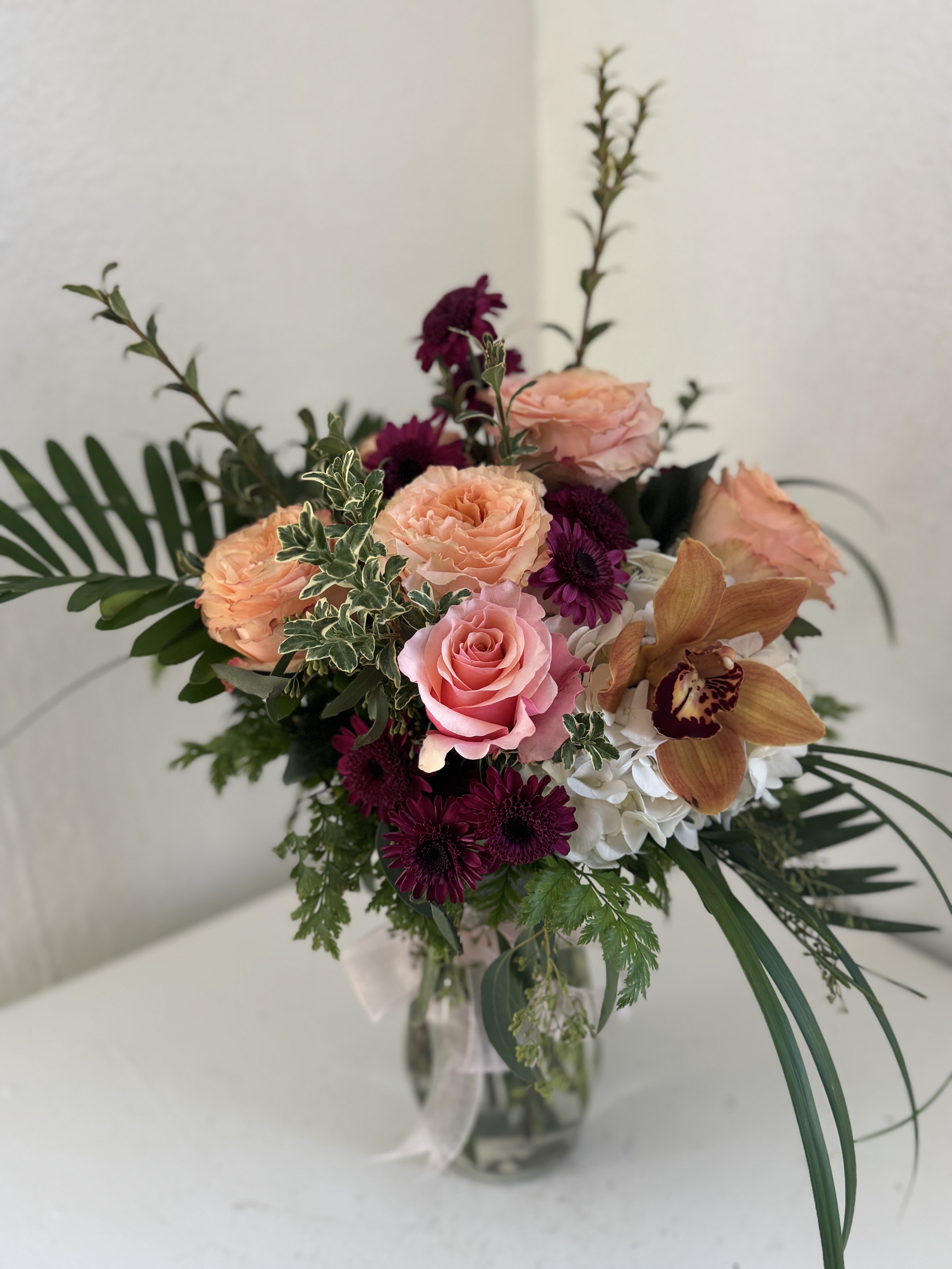 Mixed bouquet of roses, orchids, and purple blooms in a glass vase