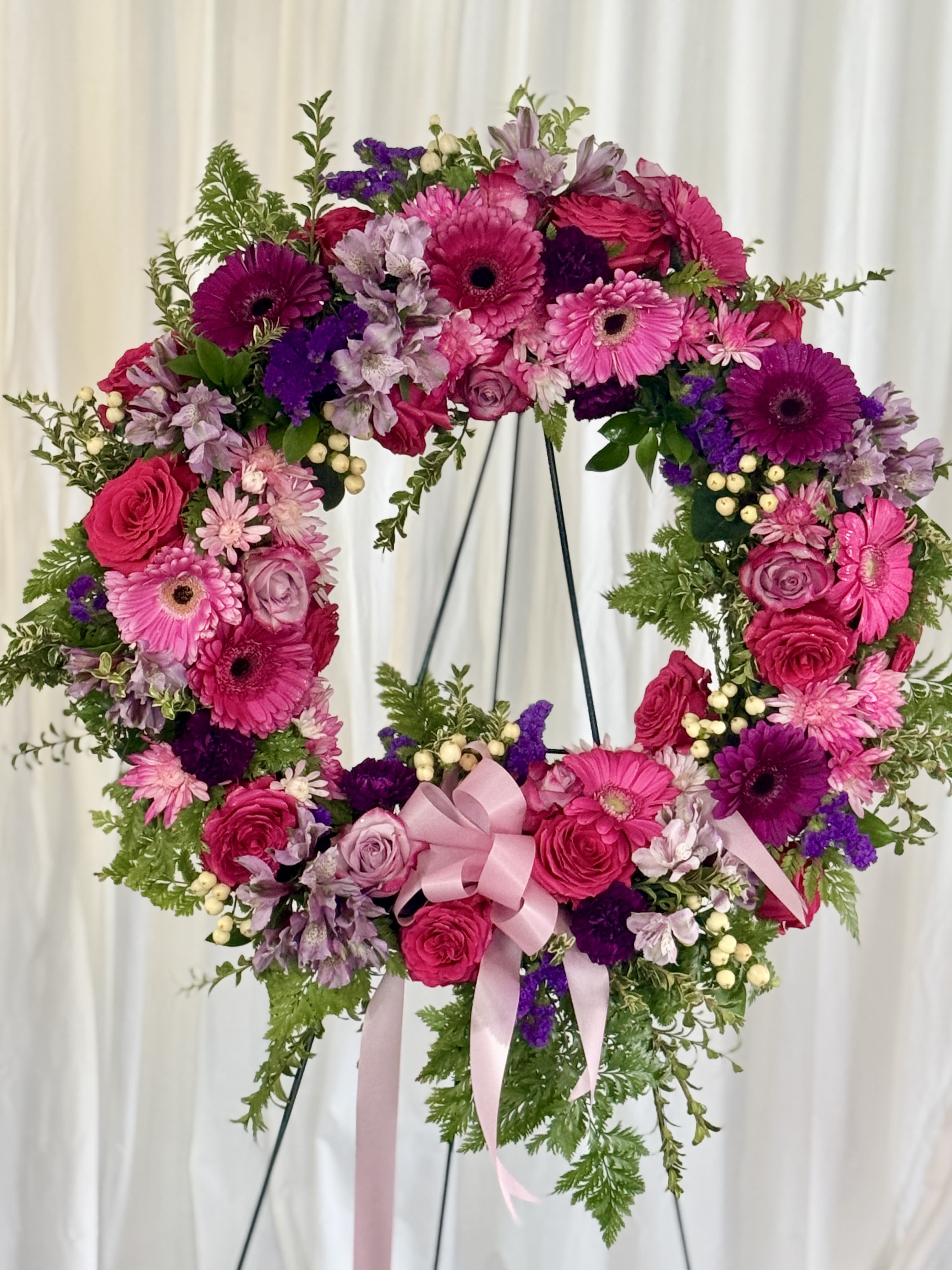 Heart-shaped floral wreath with pink and purple flowers on a stand