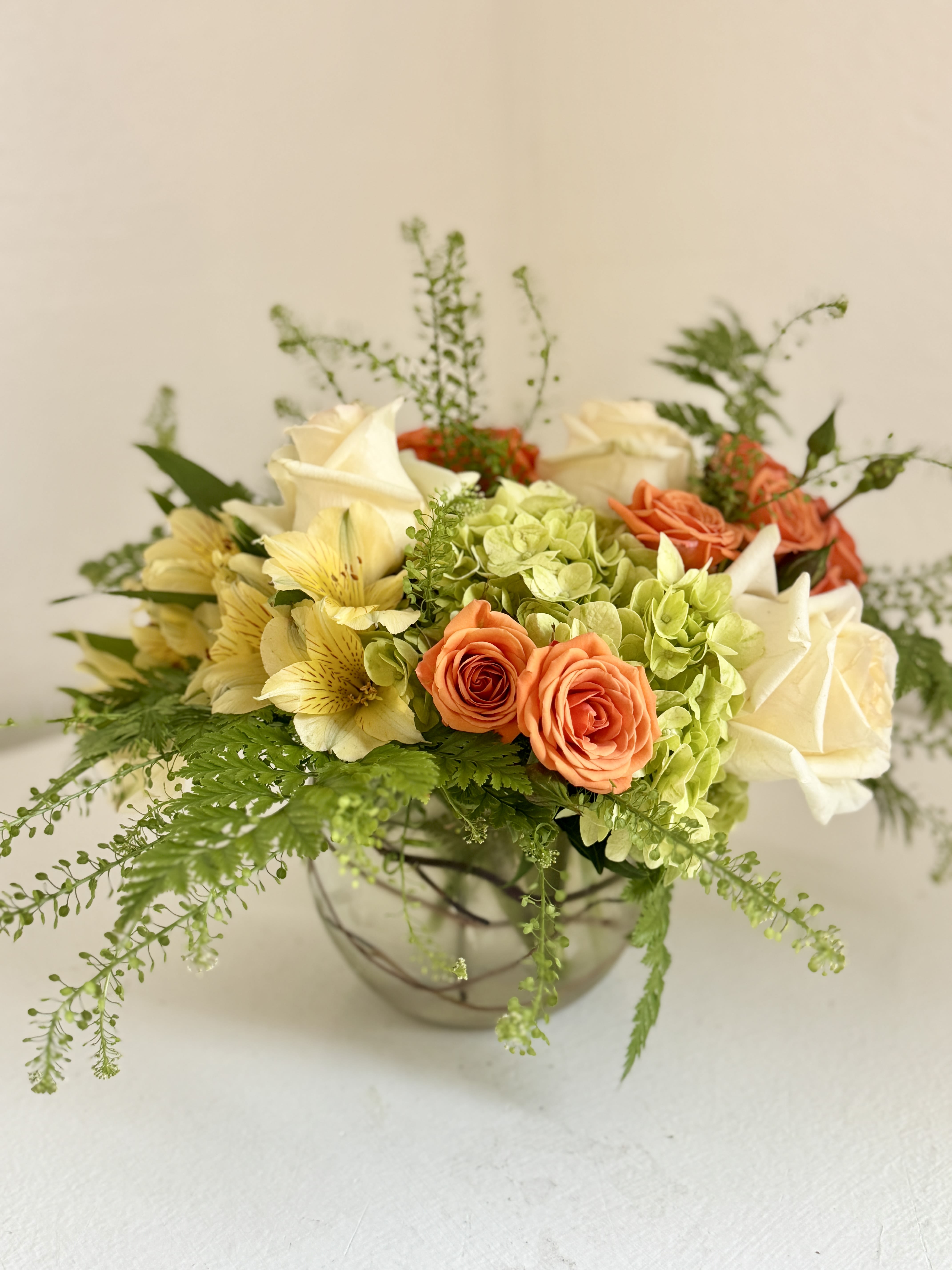 Mixed bouquet of roses, hydrangeas, and pale yellow flowers in a glass bowl vase