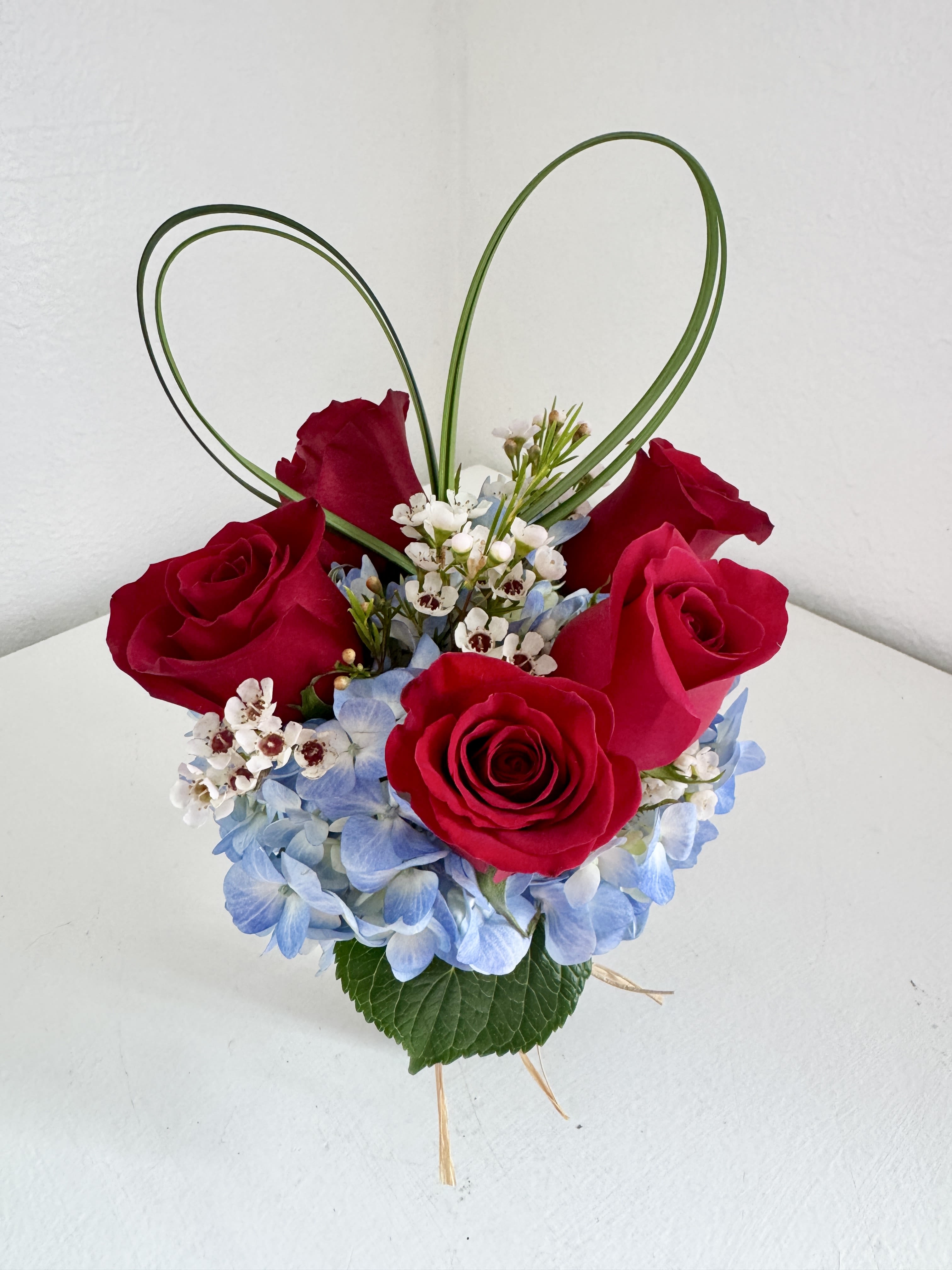 Red roses with blue hydrangea and white filler in a heart-shaped design