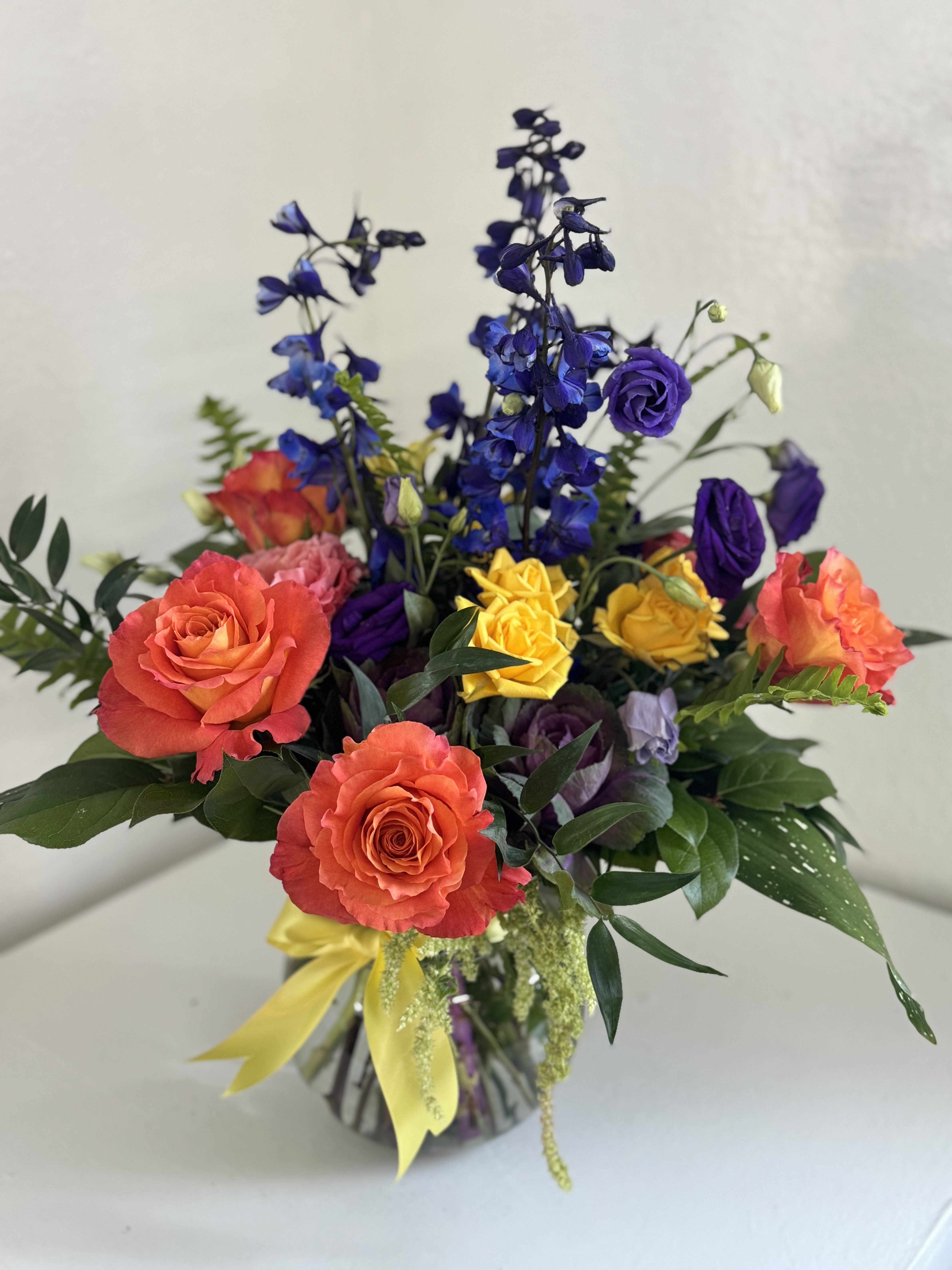 Colorful bouquet of roses and blue delphinium in a glass vase