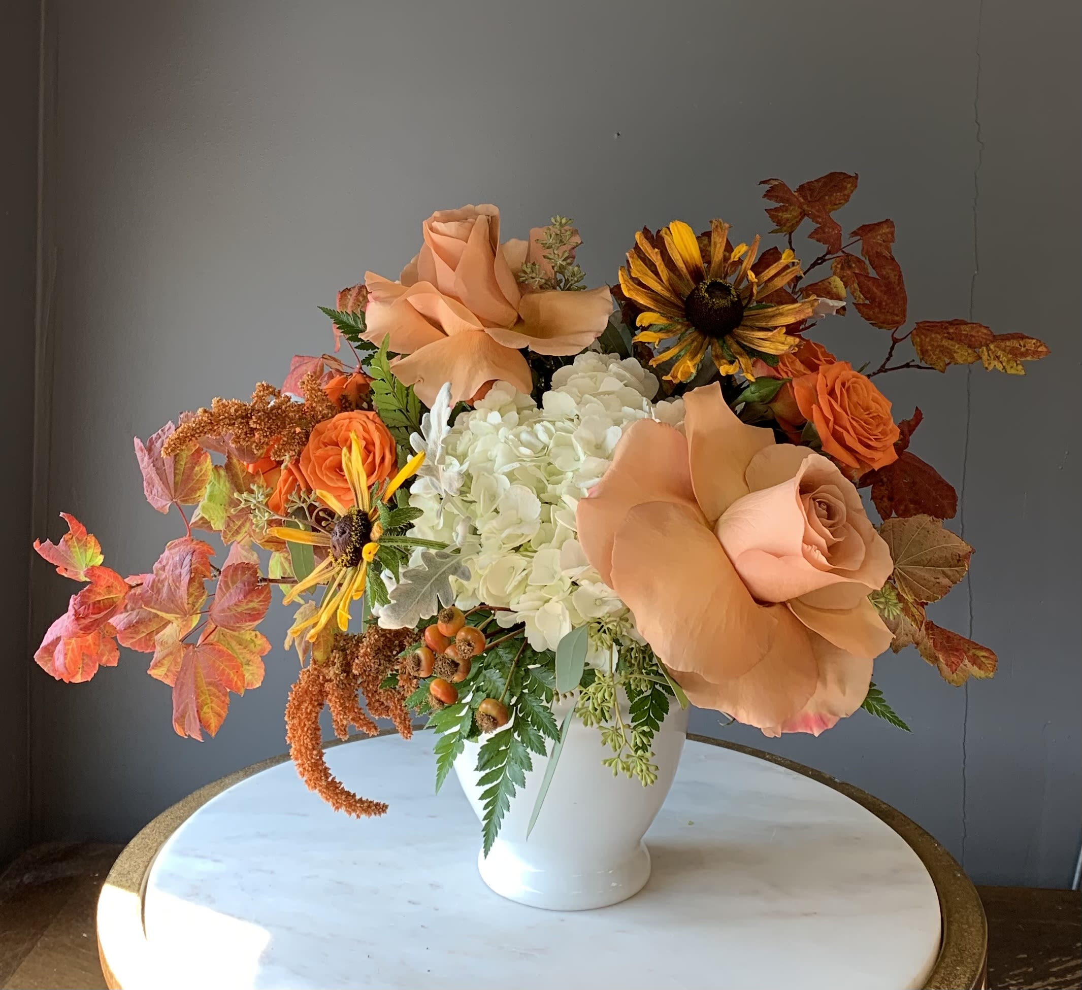Peach roses and white hydrangeas in a white vase with autumn leaves