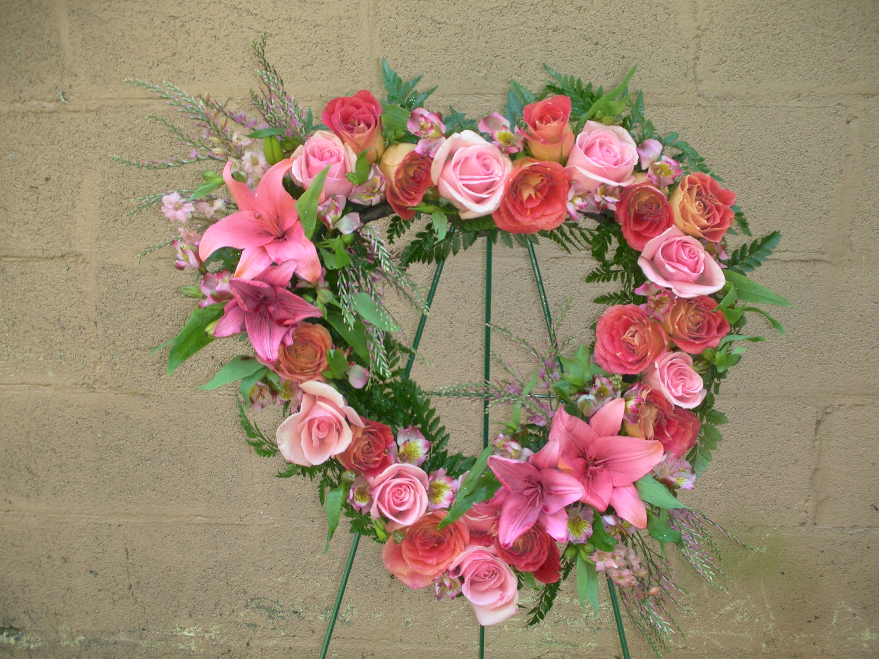 Heart-shaped floral wreath with pink roses and lilies on a stand