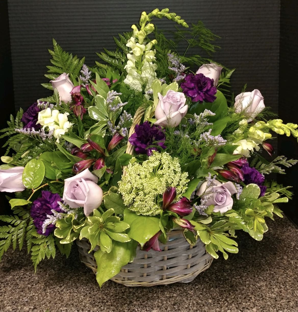 Basket arrangement of lavender roses, purple blooms, and white flowers
