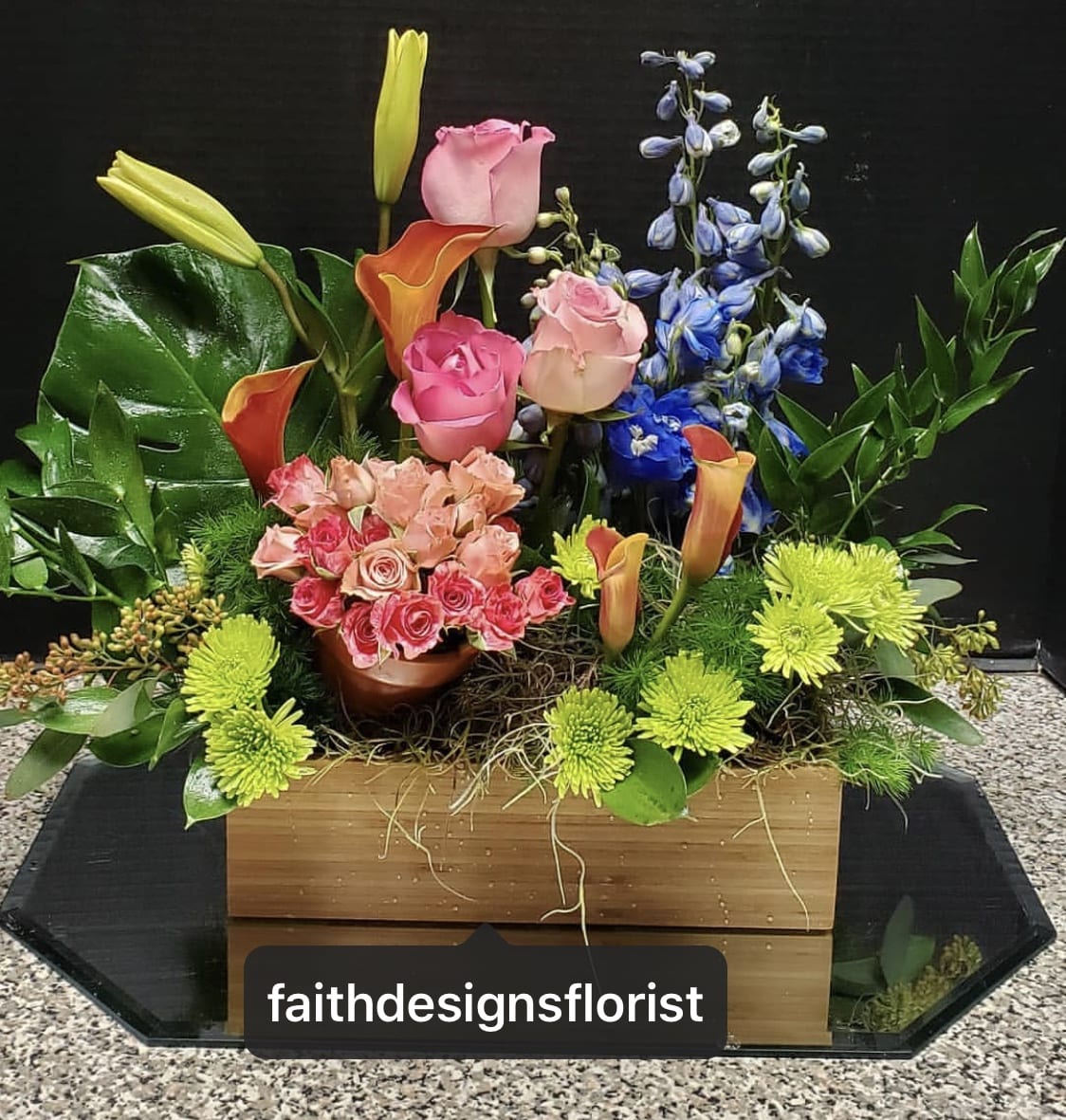 Mixed floral arrangement with roses, calla lilies, and blue delphinium in a wooden box