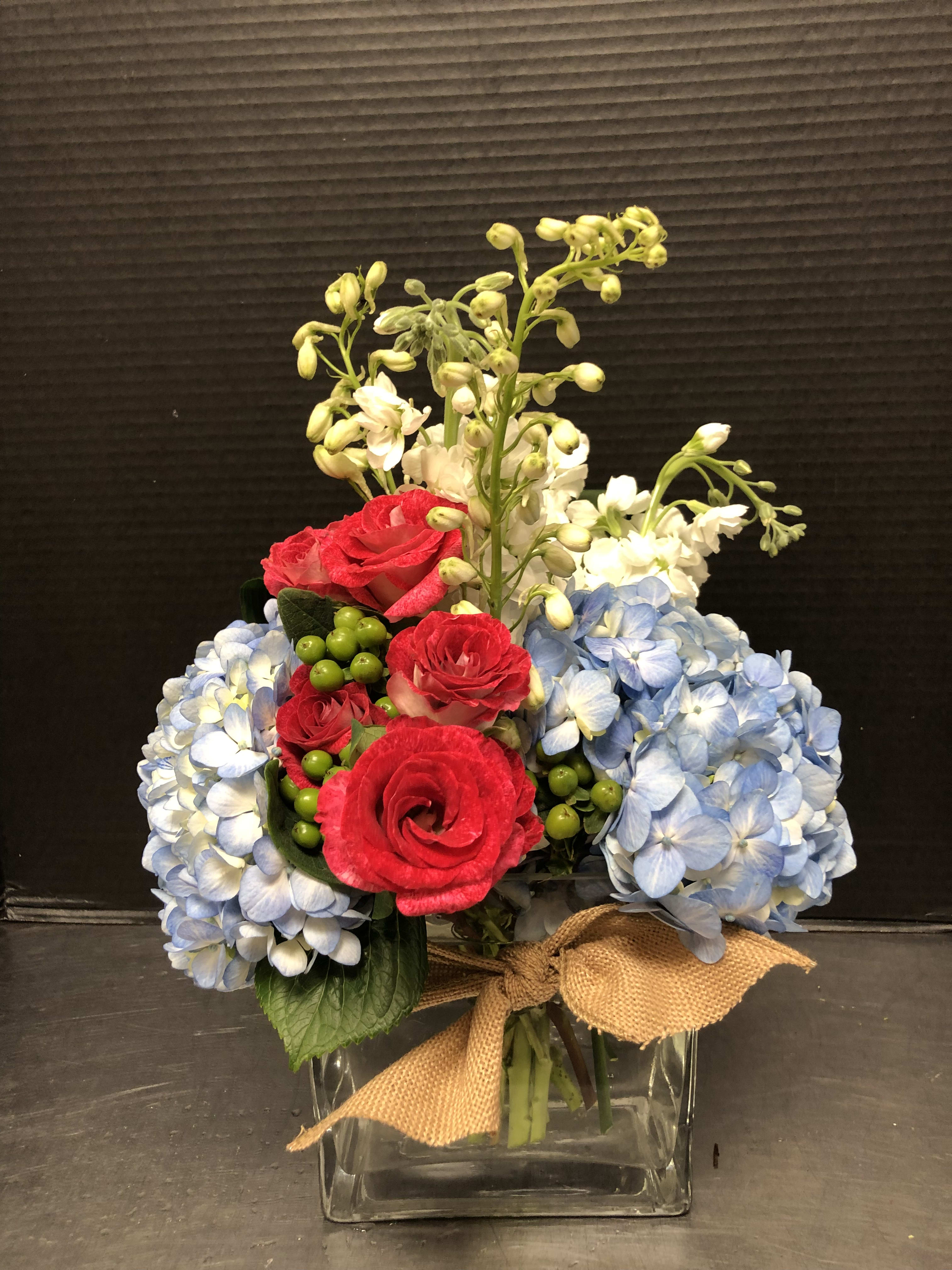 Bouquet of red roses and blue hydrangeas in a glass vase with a burlap bow