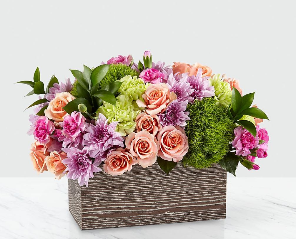 Simple Charm™ Bouquet - Capture the beauty of the seasons in bloom with our Simple Charm Bouquet. Gorgeous blooms such as peach spray roses, green trick dianthus, pink mini carnations and lavender cushion pompons fill a weathered wooden box with freshness. Whether you're saying thank you to a special friend or sharing the most heartfelt get-well message, this arrangement is a breathtaking gift for your loved ones to cherish. 