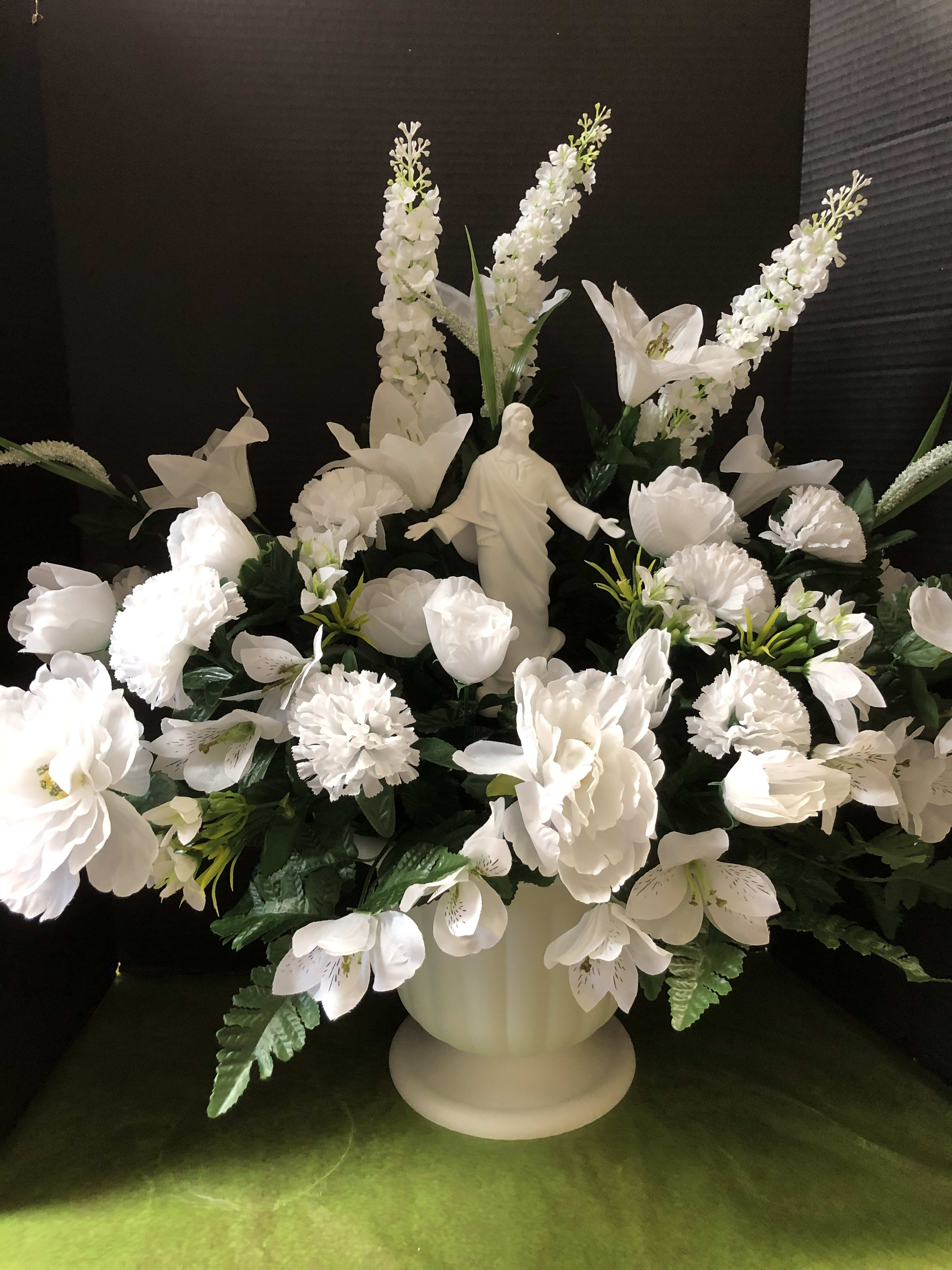 White floral arrangement with a religious statue in a pedestal vase