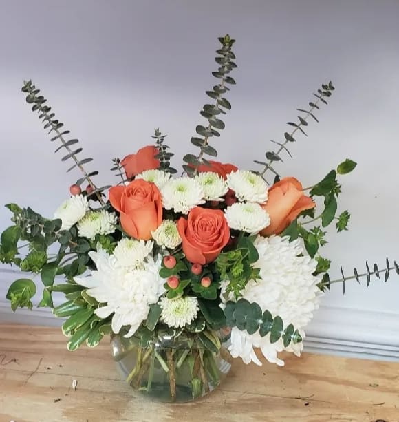 Orange roses and white chrysanthemums in a glass vase with eucalyptus