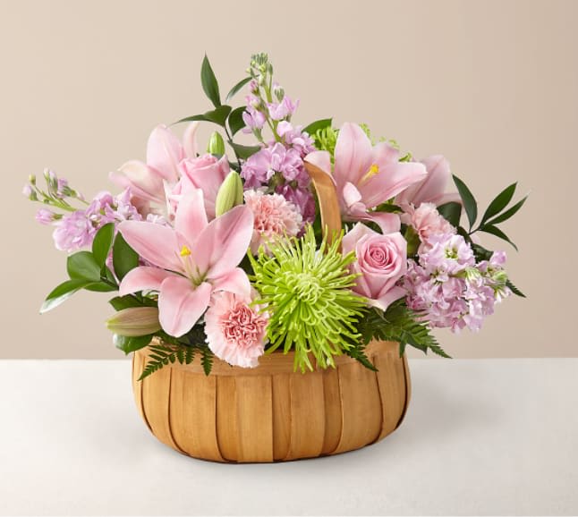 Pink lilies and roses arranged in a wooden basket with green accents