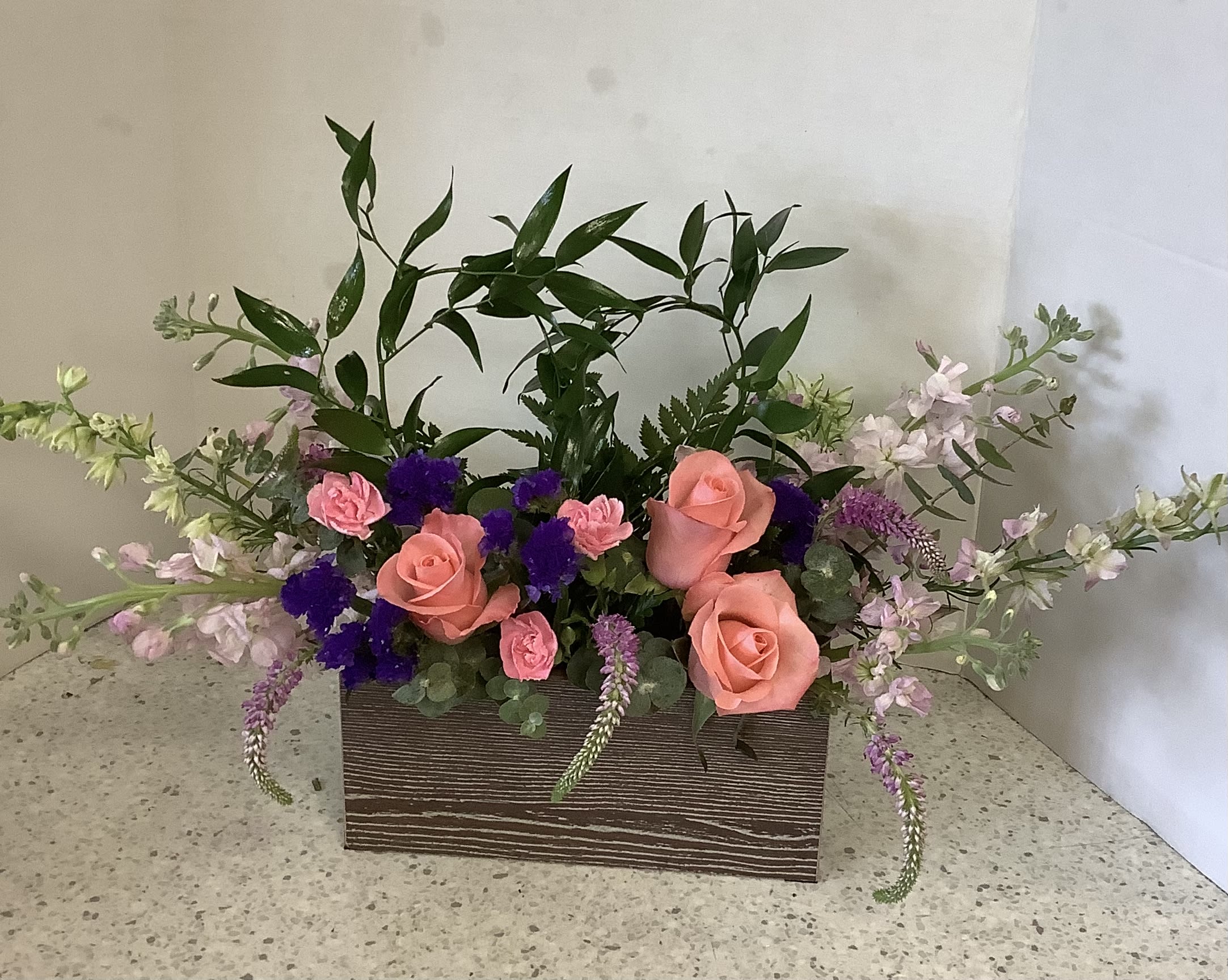 Pink roses and purple flowers arranged in a rectangular wooden box