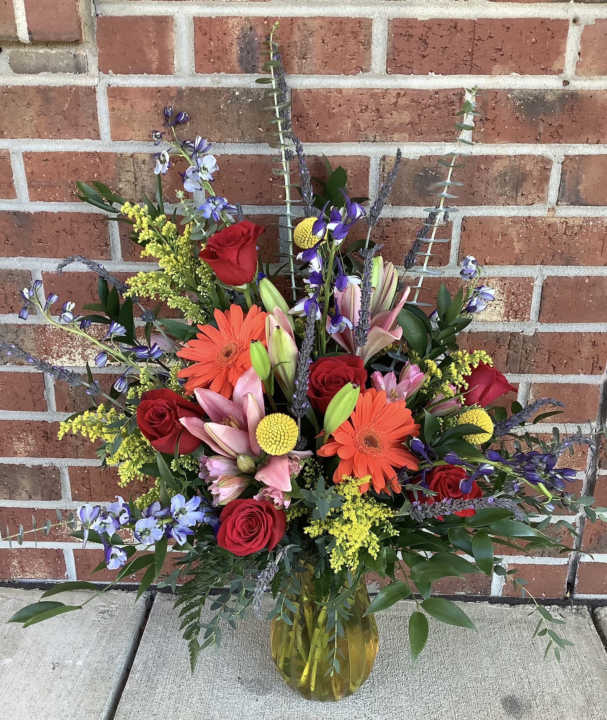 Mixed bouquet of red roses, lilies, and orange gerbera daisies in a glass vase