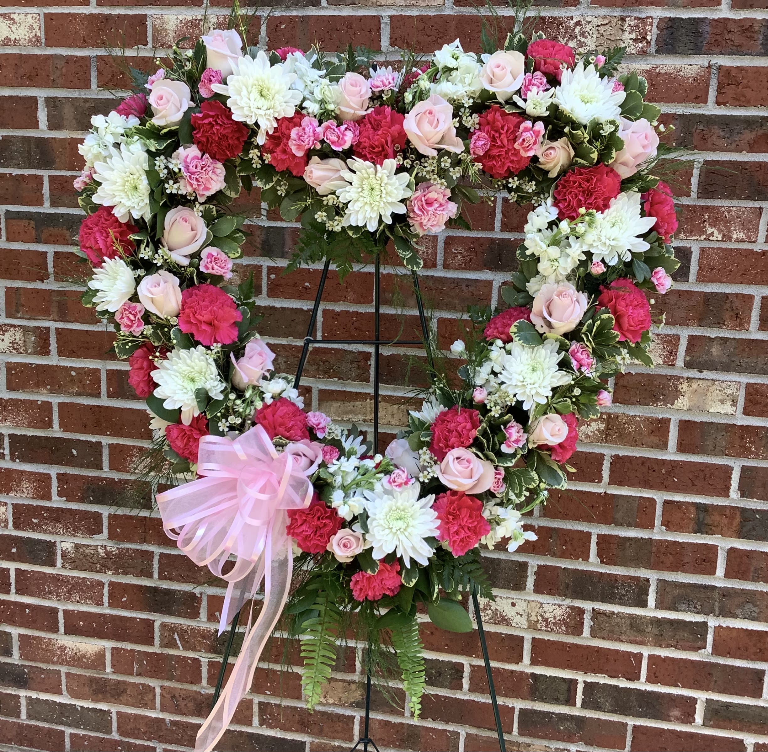 Heart-shaped floral wreath with pink and white flowers on a stand