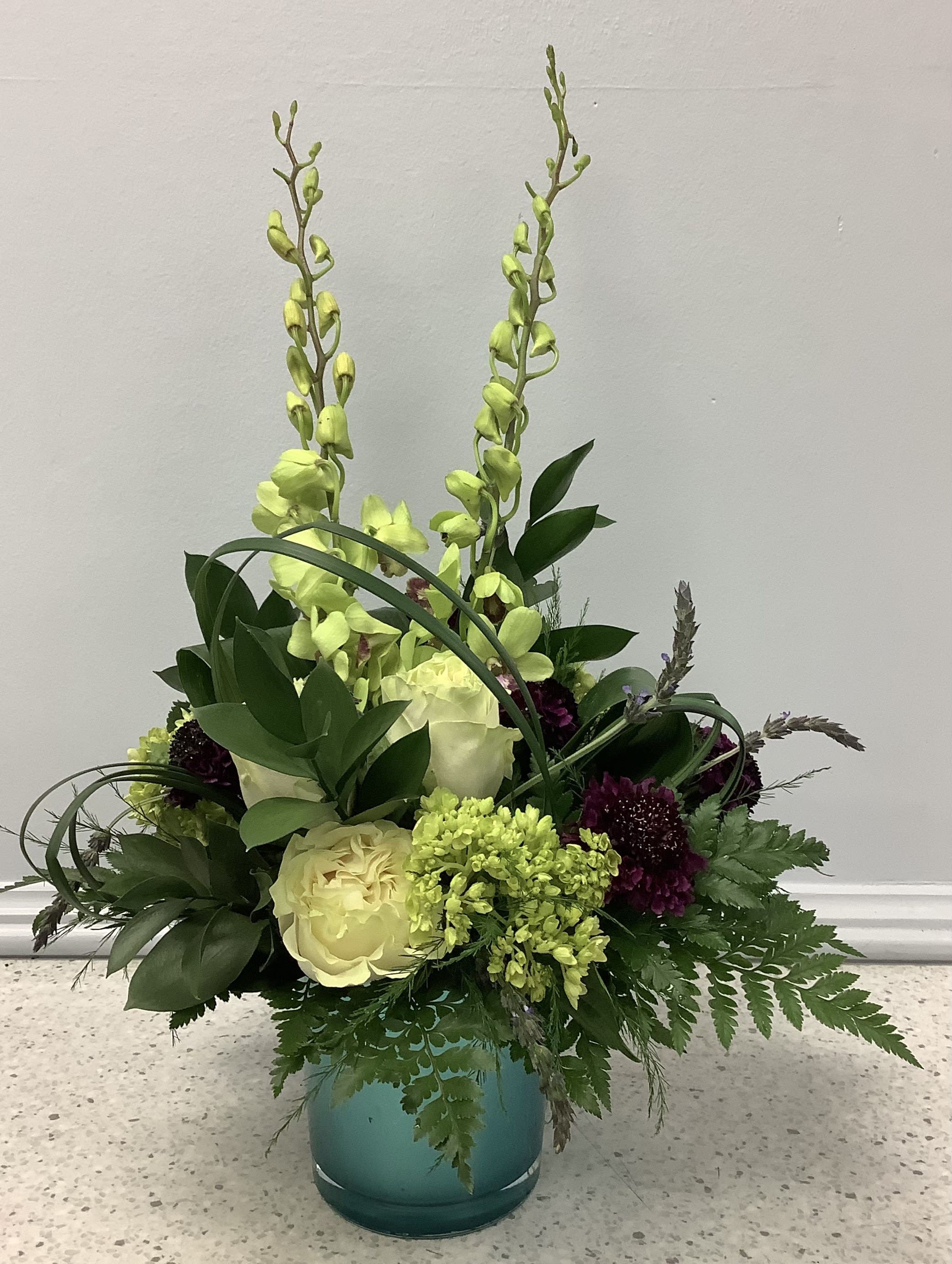 Tall floral arrangement in a teal vase with pale yellow roses and green orchids