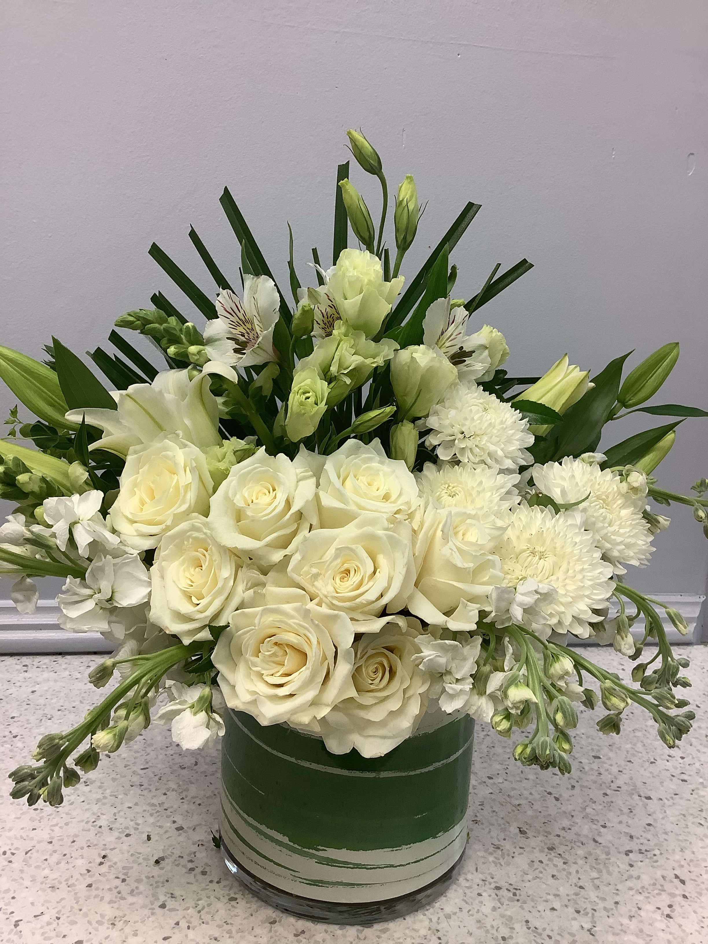 White roses and lilies arranged in a green glass vase
