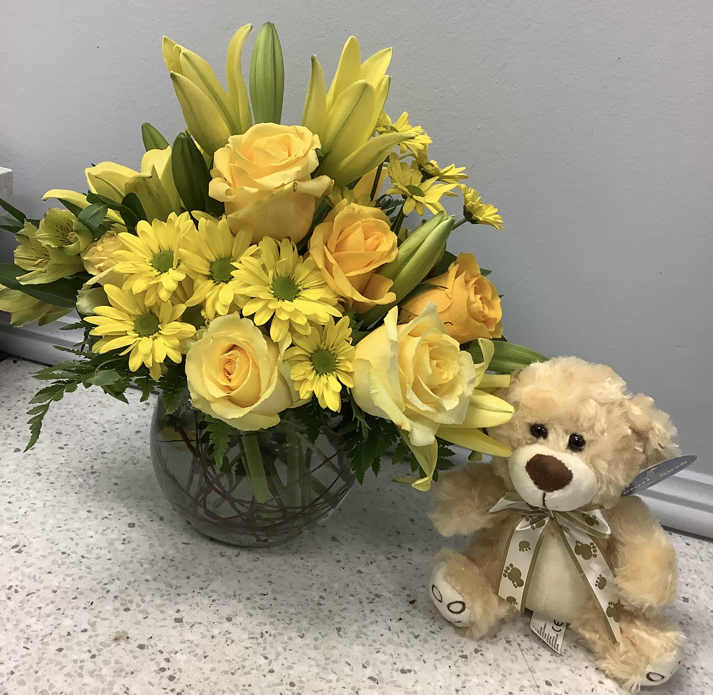 Yellow roses and daisies in a glass vase beside a teddy bear