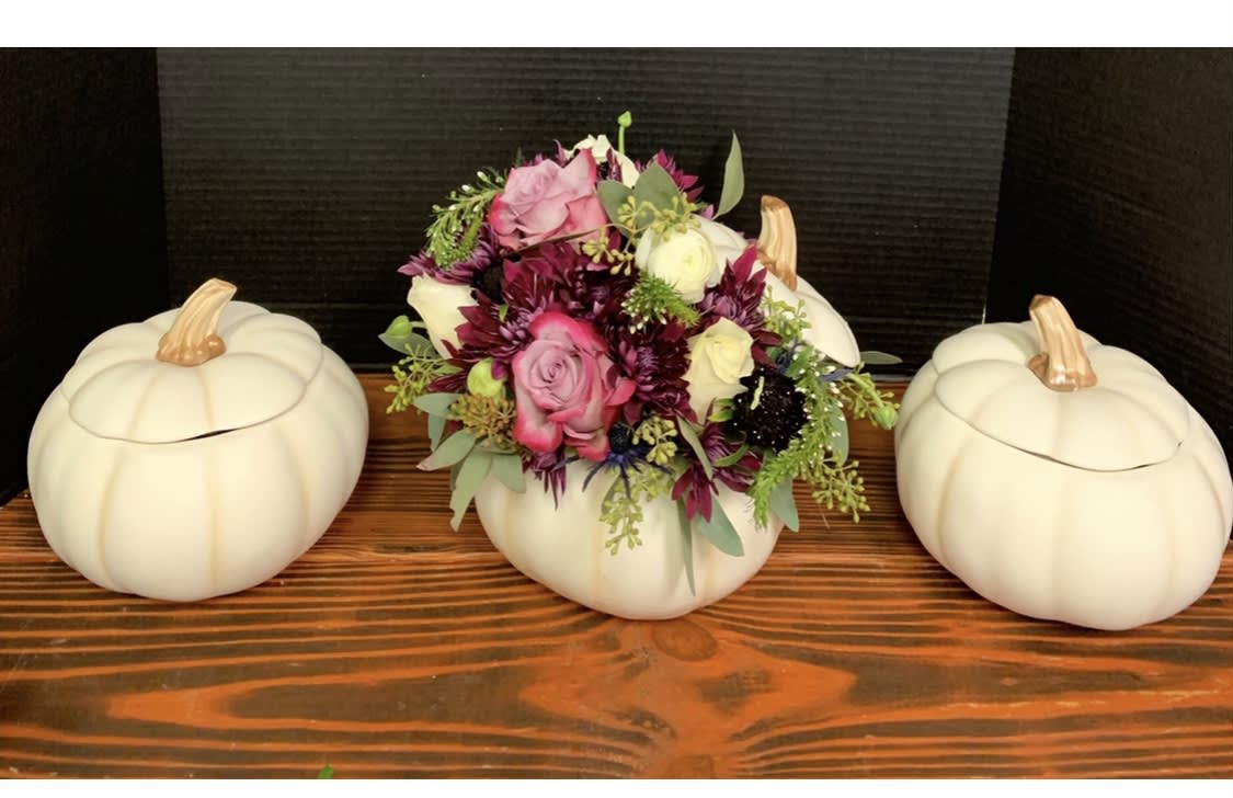 Floral arrangement in a white pumpkin container flanked by two matching pumpkins