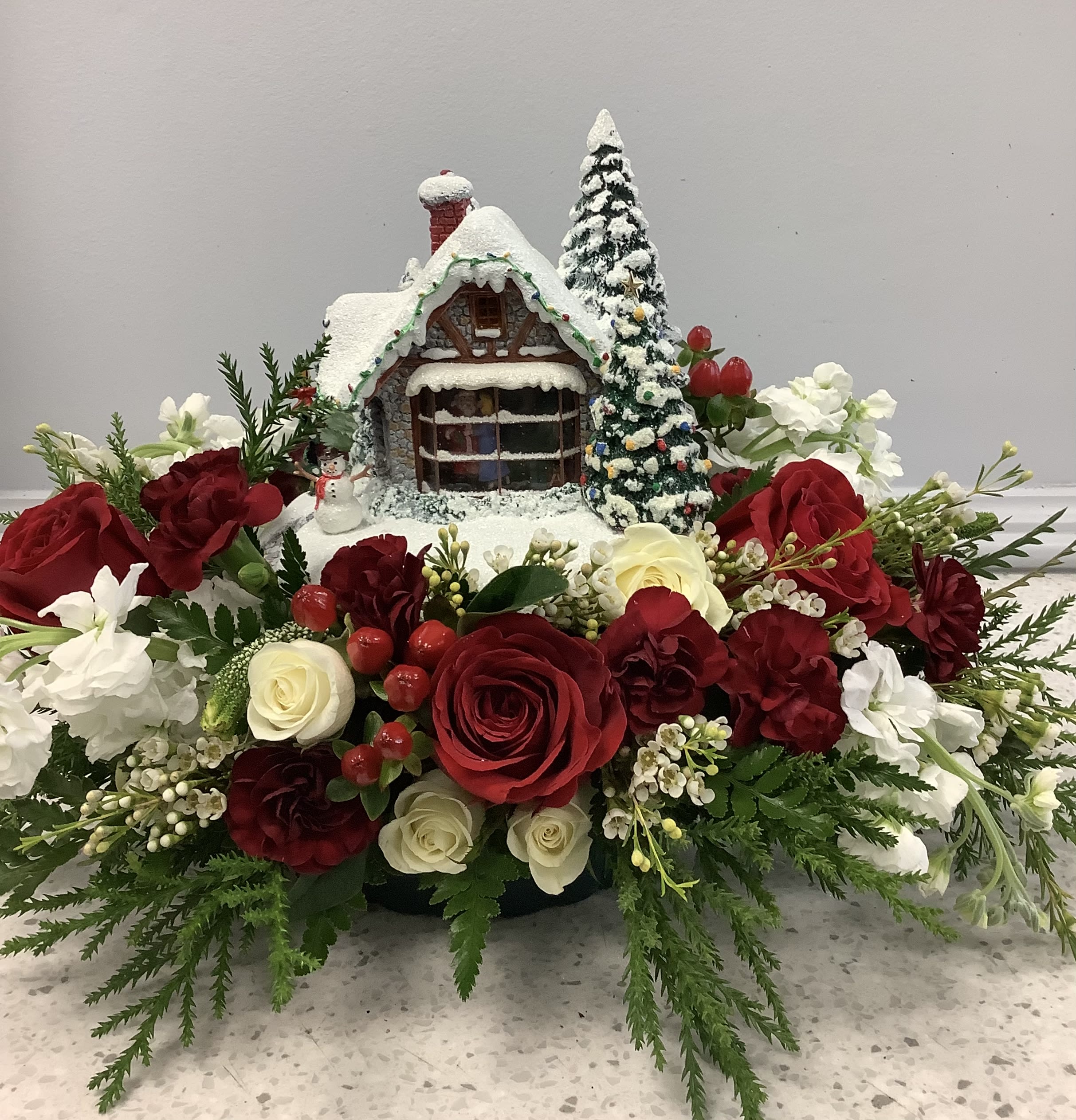 Christmas floral arrangement with red and white roses around a snowy house centerpiece