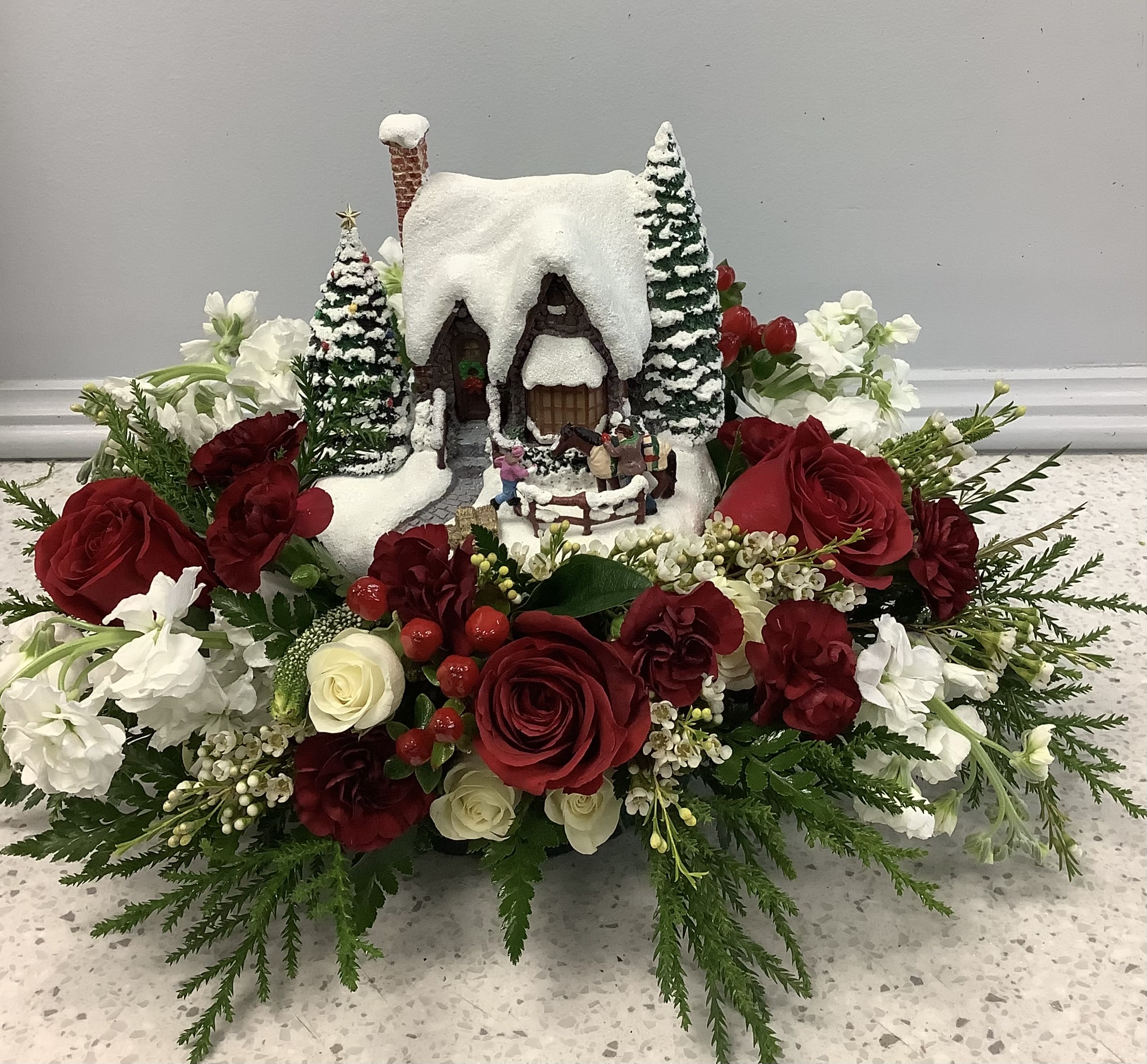 Winter floral arrangement with a snowy cottage centerpiece and red and white roses