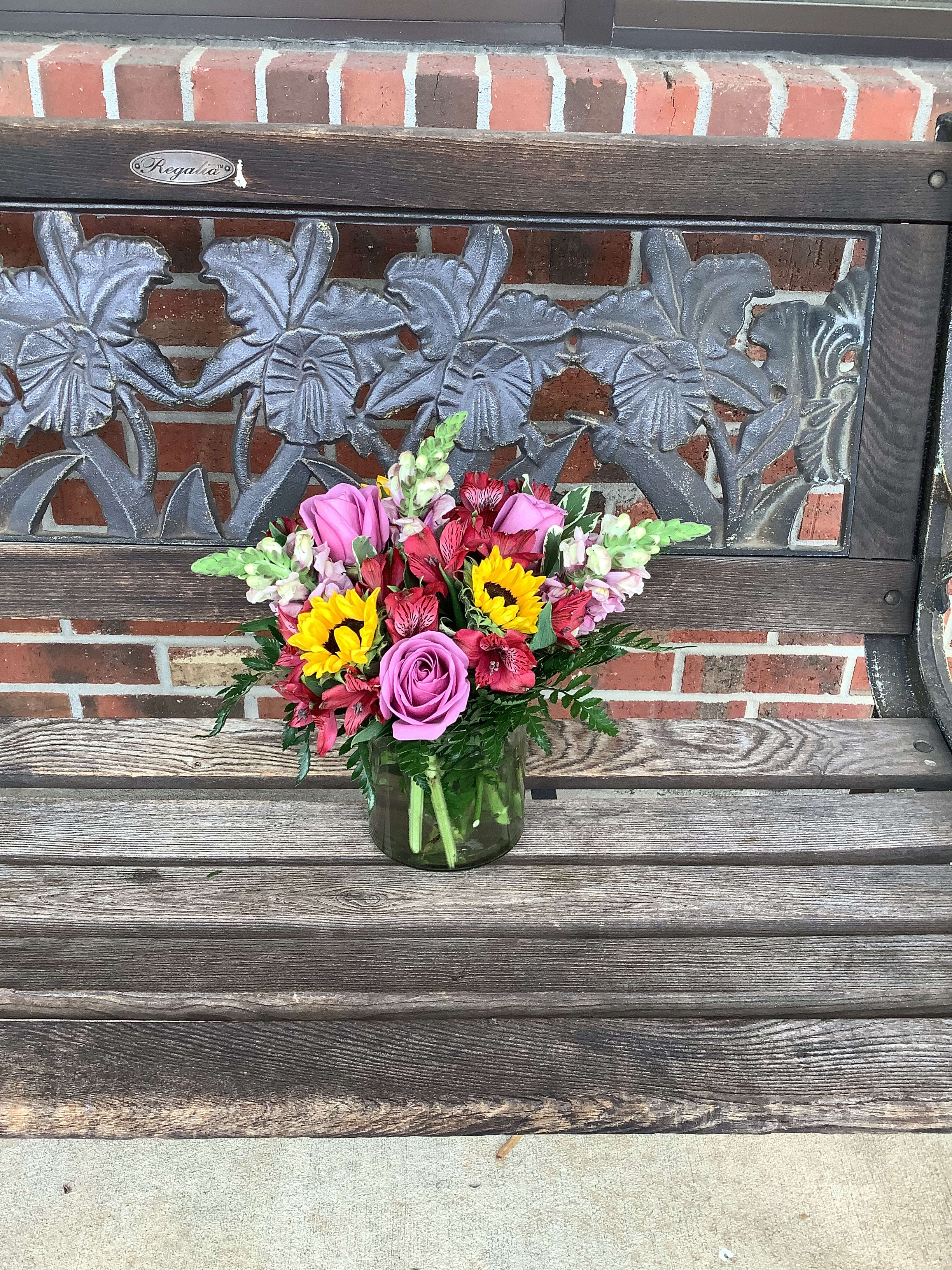 Mixed bouquet of pink roses, sunflowers, and red flowers in a glass vase
