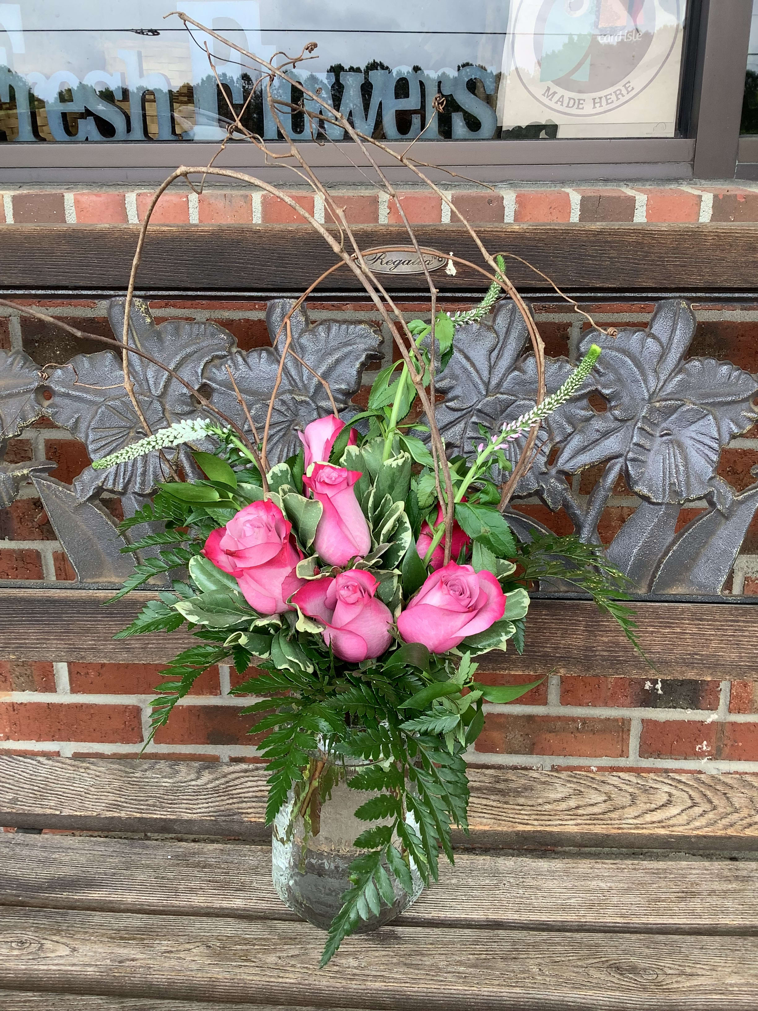 Pink roses arranged in a glass vase with branches and greenery