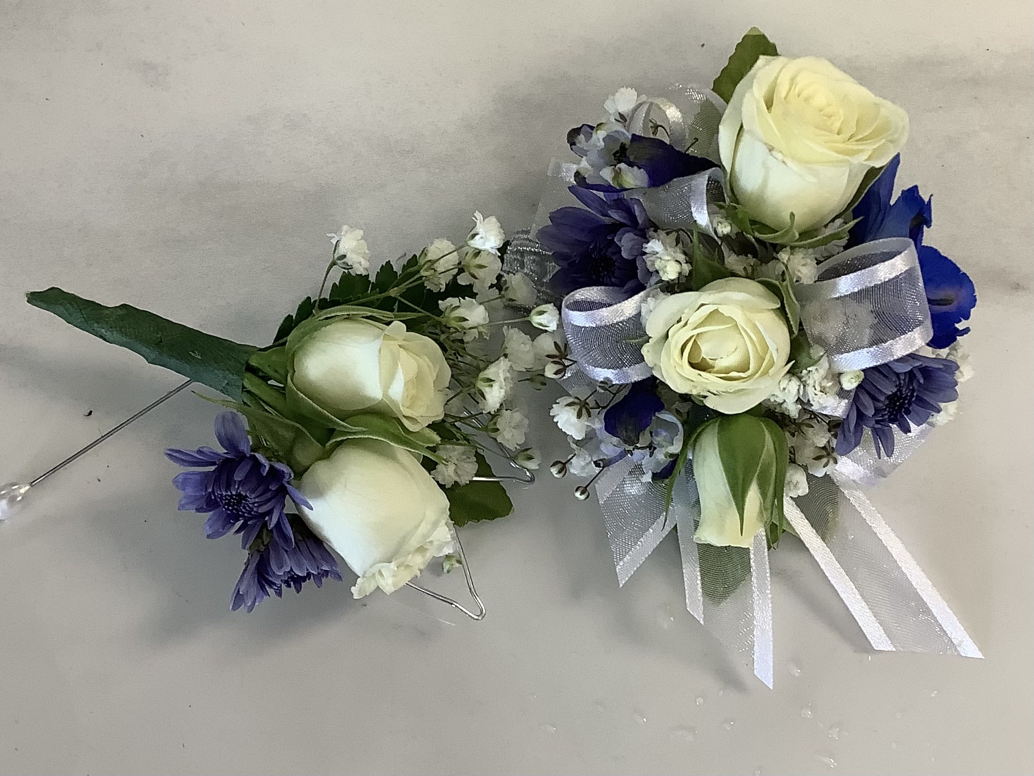 Two small floral corsages with white roses and purple flowers, tied with silver ribbon.
