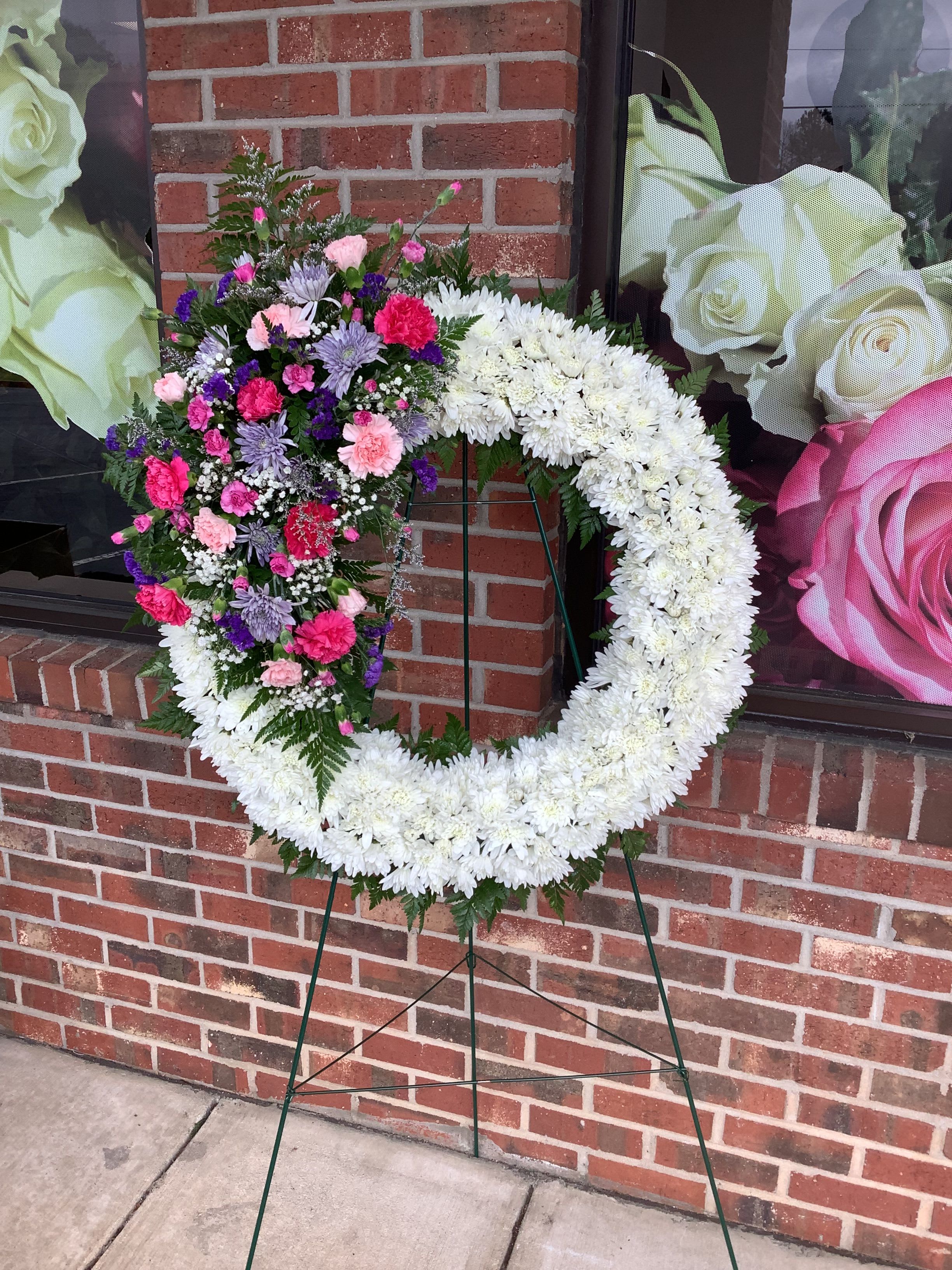 Heart-shaped floral wreath on a stand with white and mixed pink-purple flowers