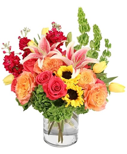 Mixed bouquet of roses, lilies, sunflowers, and red blooms in a glass vase