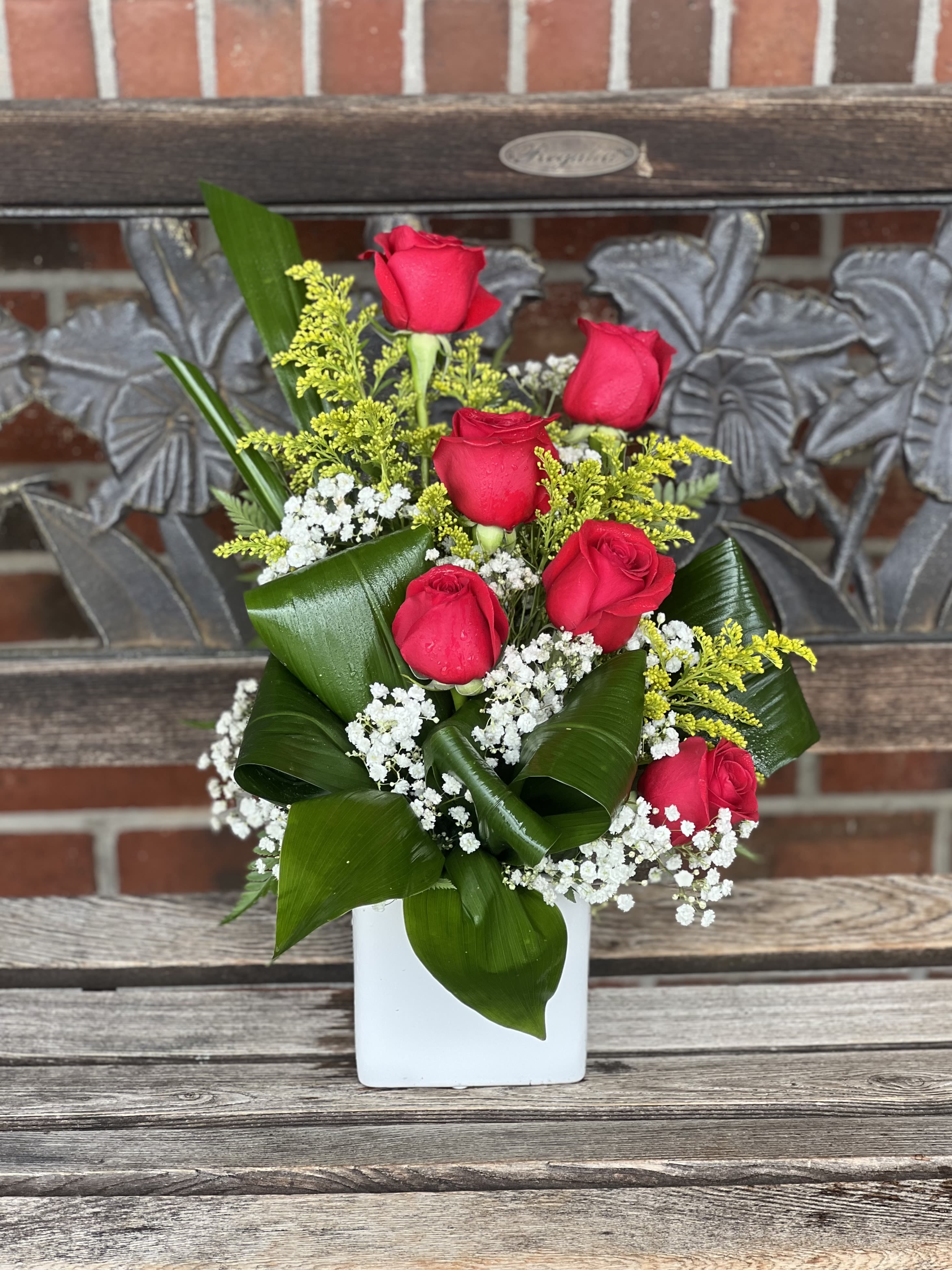 Red roses arranged in a white vase with baby's breath and greenery