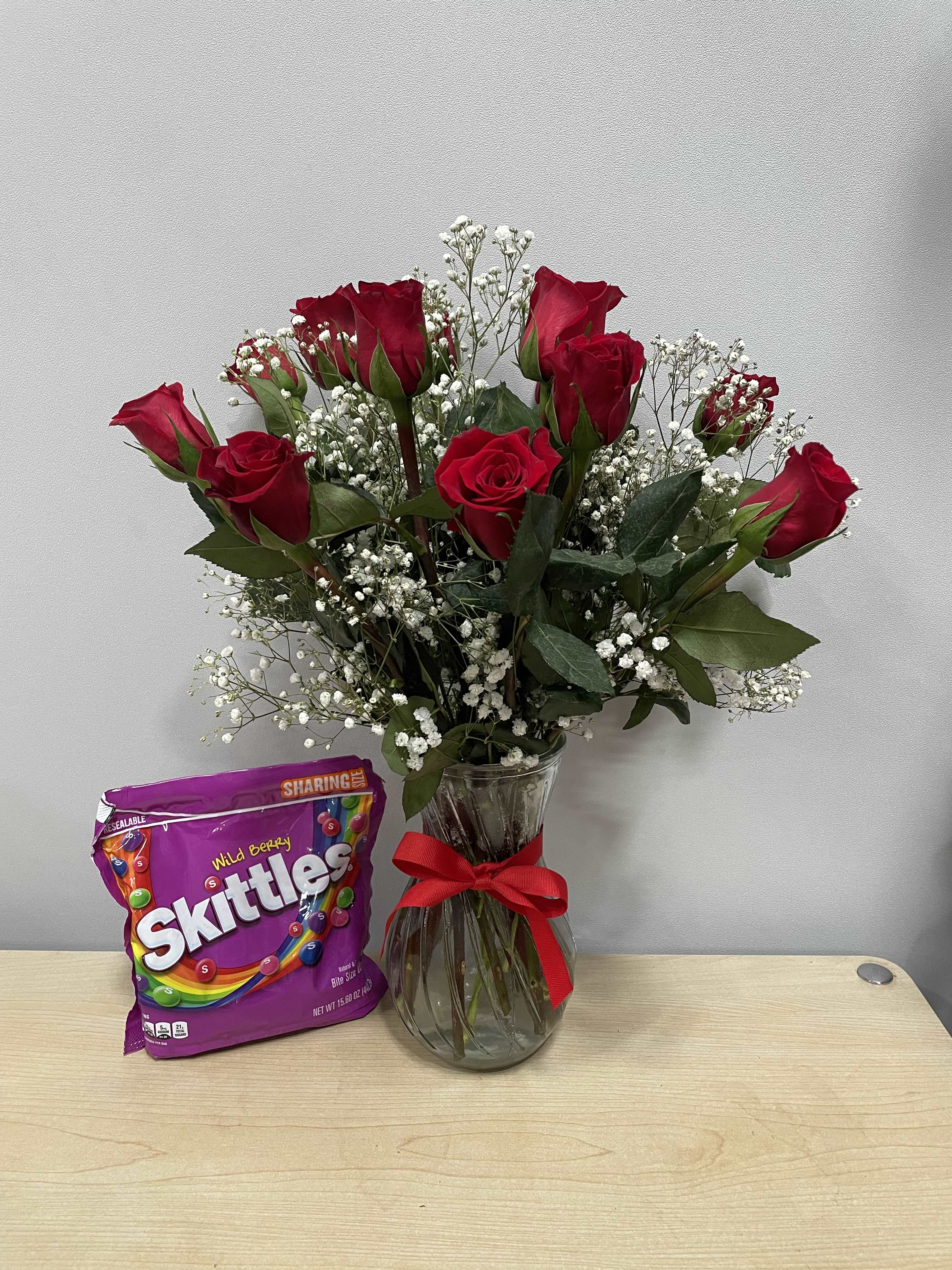 Red roses in a glass vase with a bag of Skittles candy