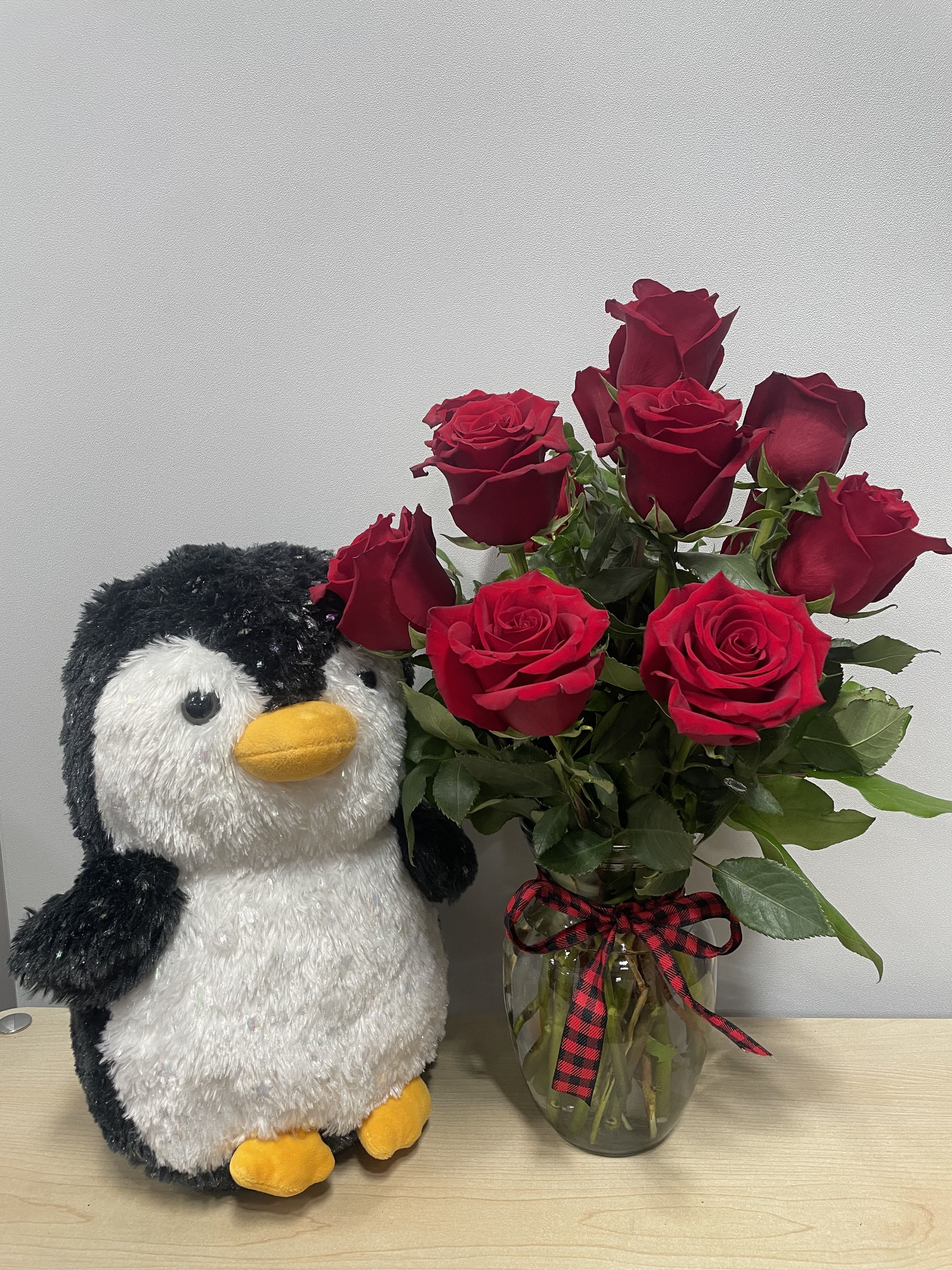 Red roses in a glass vase beside a plush penguin