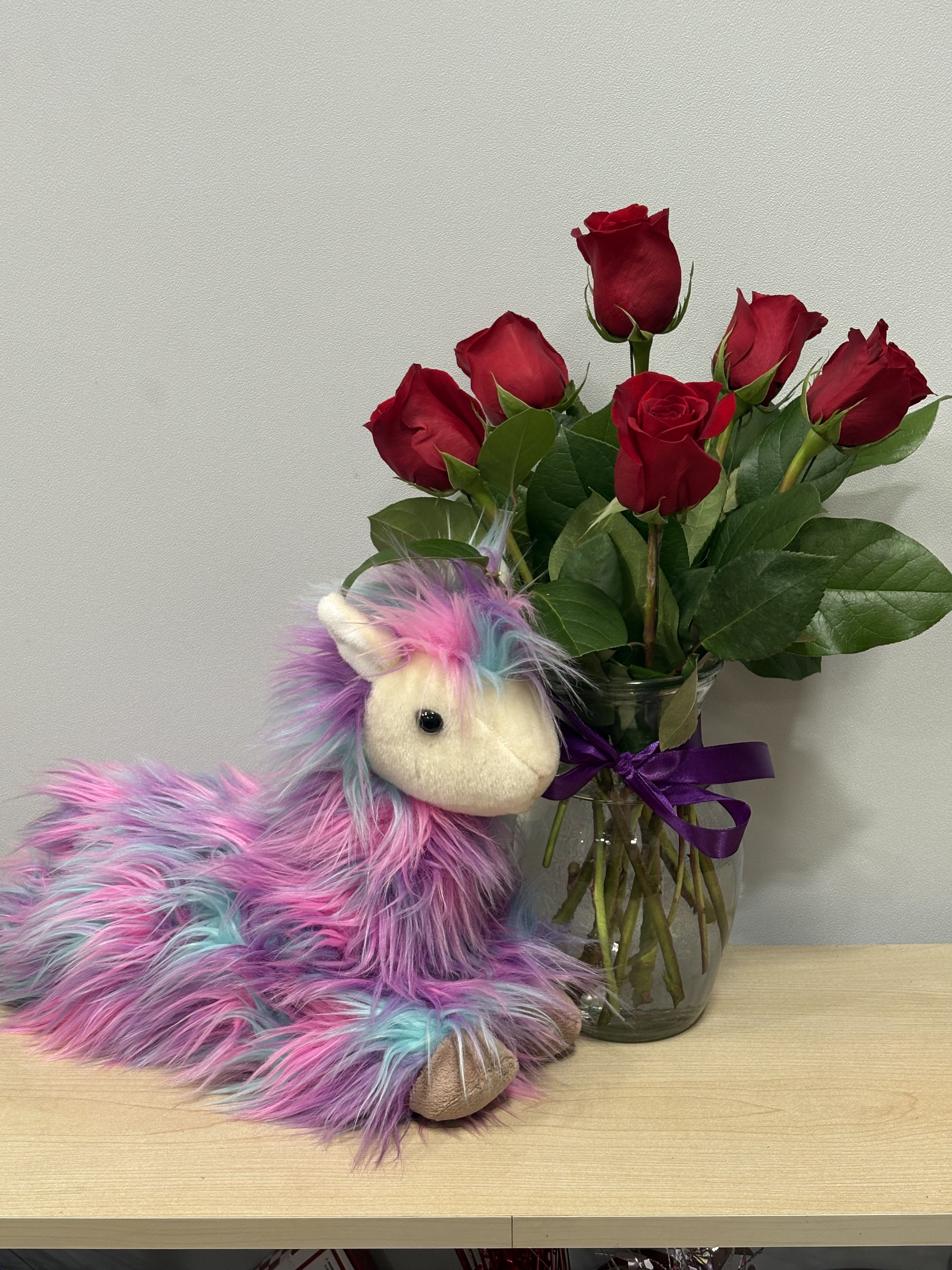 Red roses in a glass vase beside a colorful plush unicorn