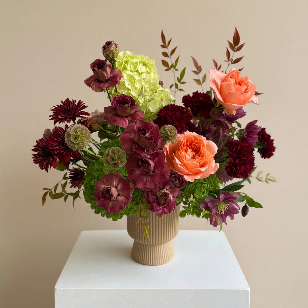 Mixed floral arrangement in a ribbed beige vase with peach and burgundy blooms