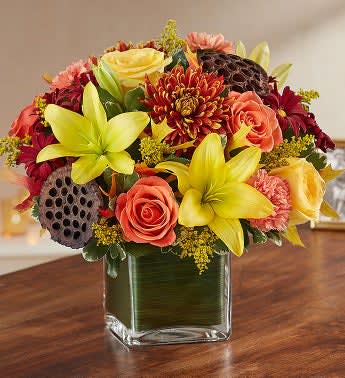 Mixed bouquet of yellow lilies, roses, and mums in a square glass vase