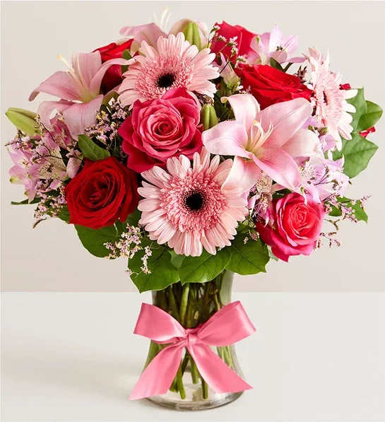 Fields of Europe Romance Bouquet - All-around arrangement with red and hot pink roses, pink Asiatic lilies, Peruvian lilies (alstroemeria), Gerbera daisies and limonium; accented with assorted greenery Artistically designed in a clear glass vase accented with a pink satin ribbon; measures 8"H vase.