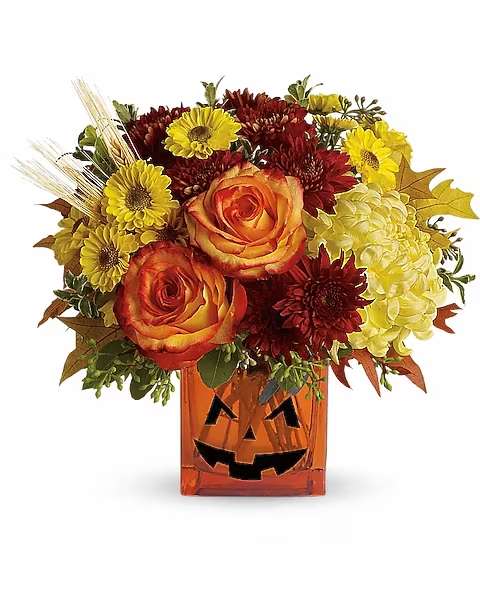 Teleflora's Halloween Glow - As colorful as Halloween candy! Yellow chrysanthemums are accented with bright orange roses and finished with eucalyptus and autumn oak leaves. All in an orange cube adorned with a jack-o-lantern face that'll brighten and frighten! This bright bouquet includes yellow cushion spray chrysanthemums, bi-color orange roses, rust cushion spray chrysanthemums, yellow disbud chrysanthemums, yellow viking spray chrysanthemums, oregonia, eucalyptus and autumn oak leaves.   