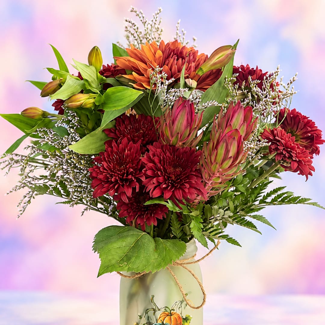 Mixed bouquet of red and orange flowers in a frosted vase with a twine bow