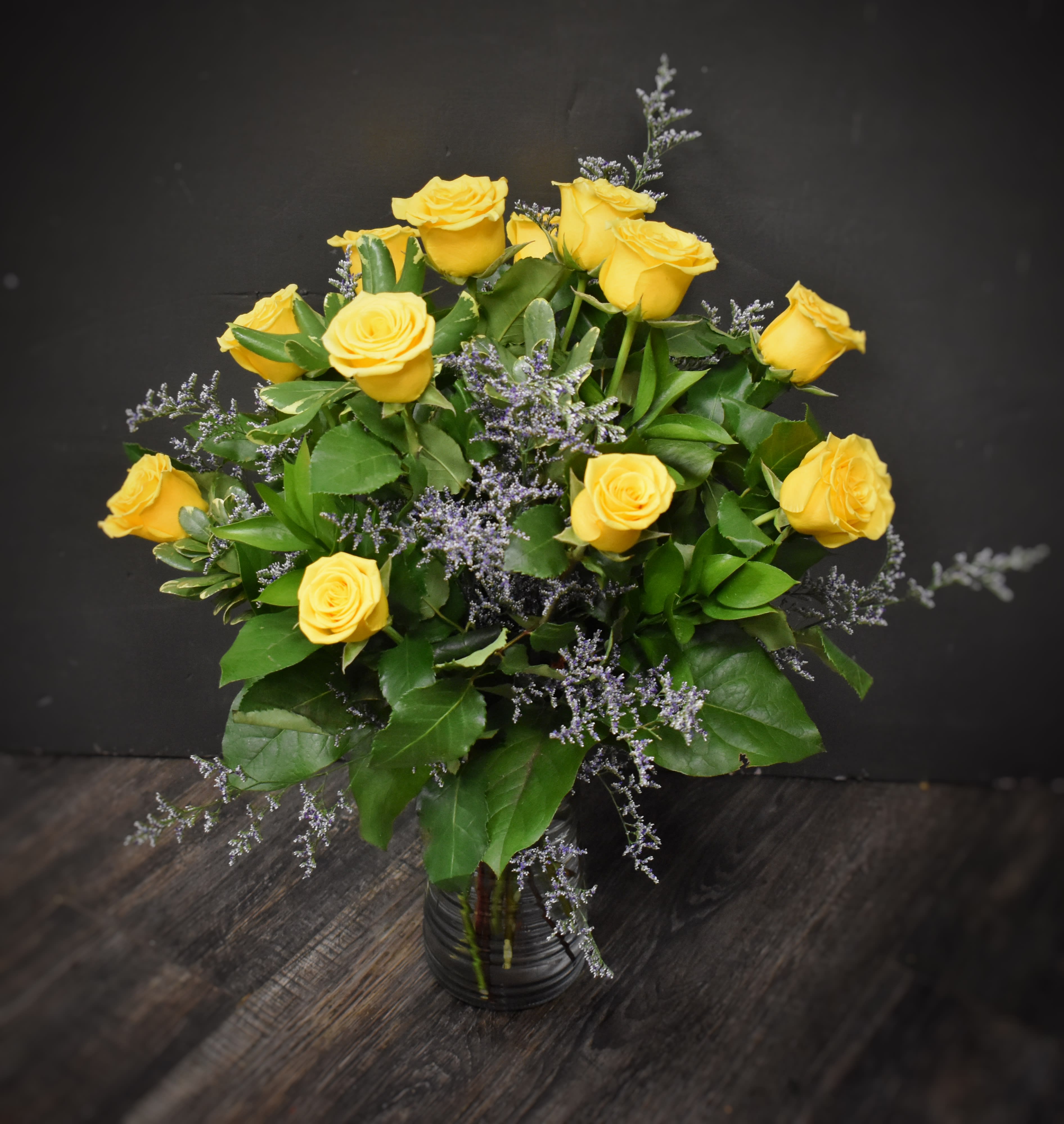 Arrangement of yellow roses with soft purple filler in a clear glass vase