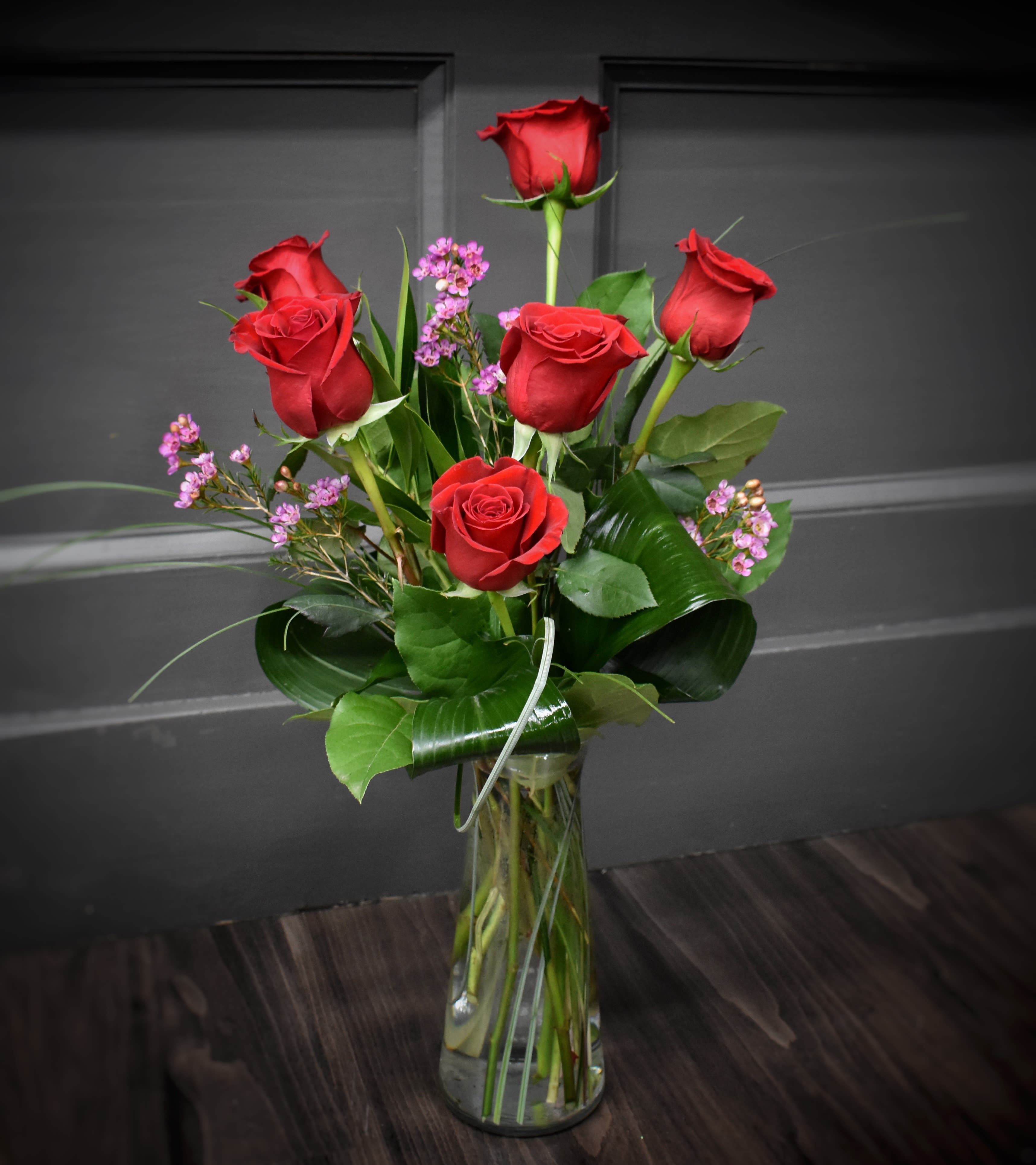 Red roses with small purple filler flowers in a clear glass vase