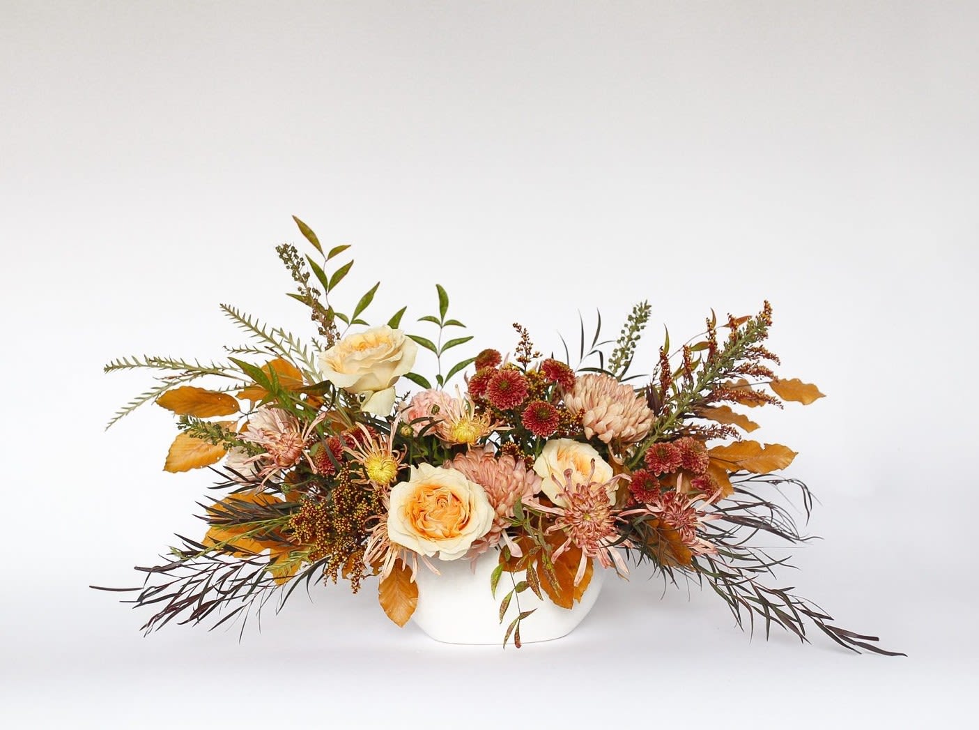 Autumn floral arrangement in a white vase with cream roses and mums