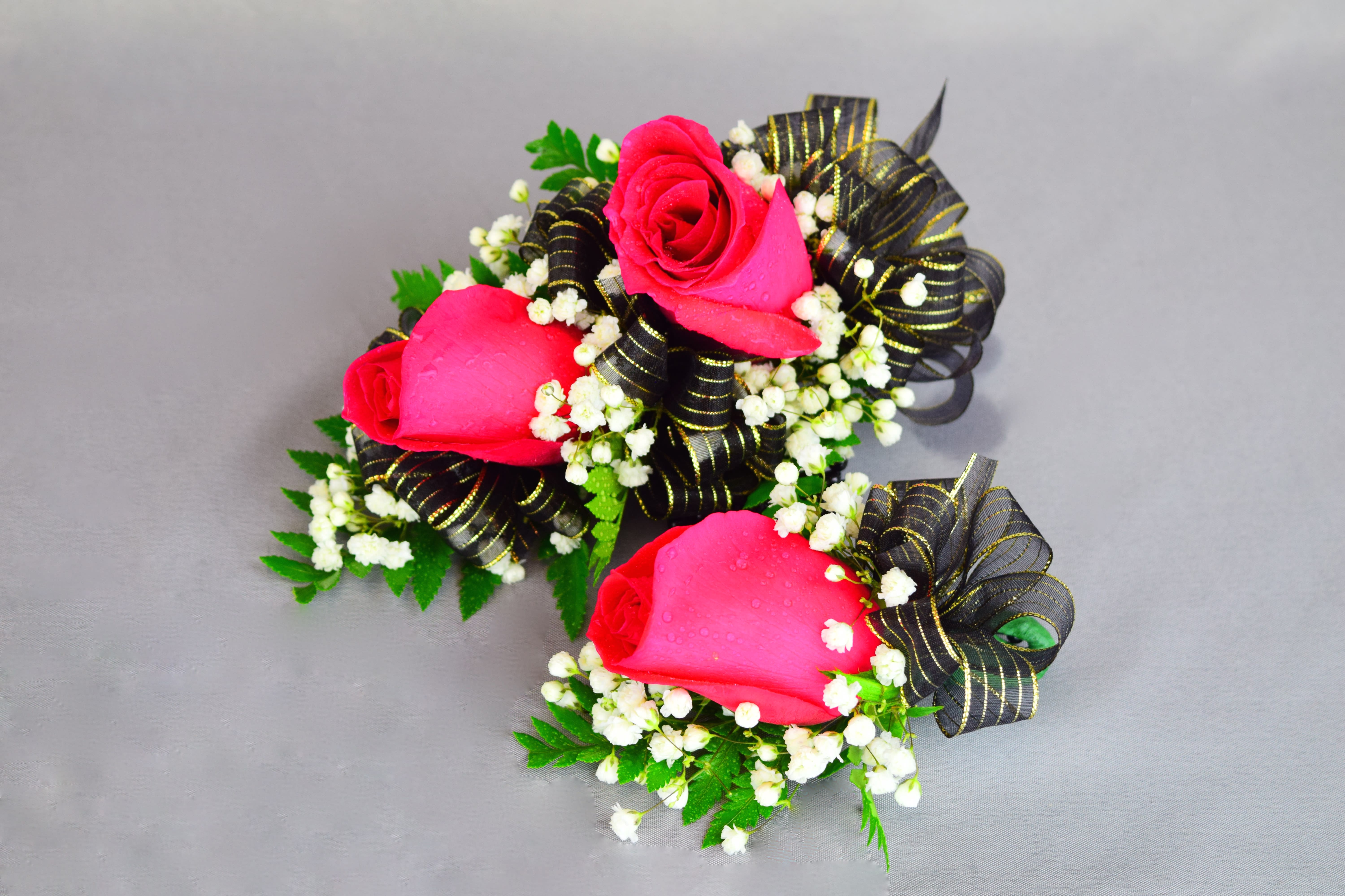 Two pink rose corsages with black ribbon and white filler flowers