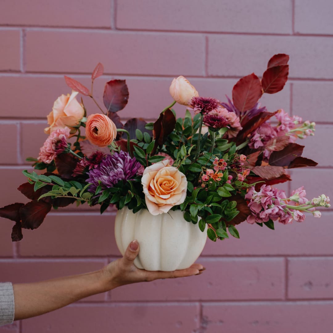 Peach and purple floral arrangement in a white pumpkin vase