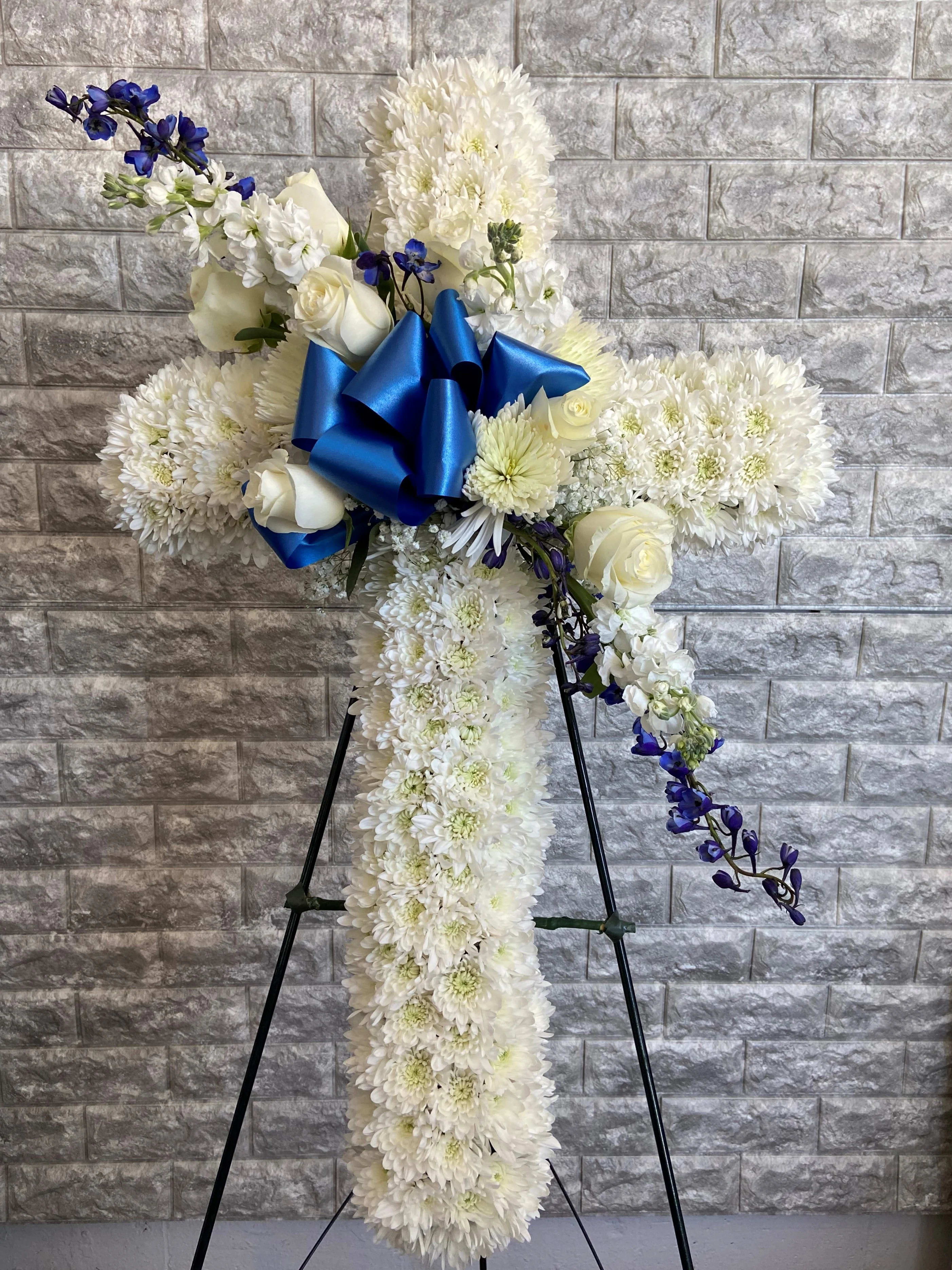 White floral standing spray with blue ribbon and purple accents on an easel