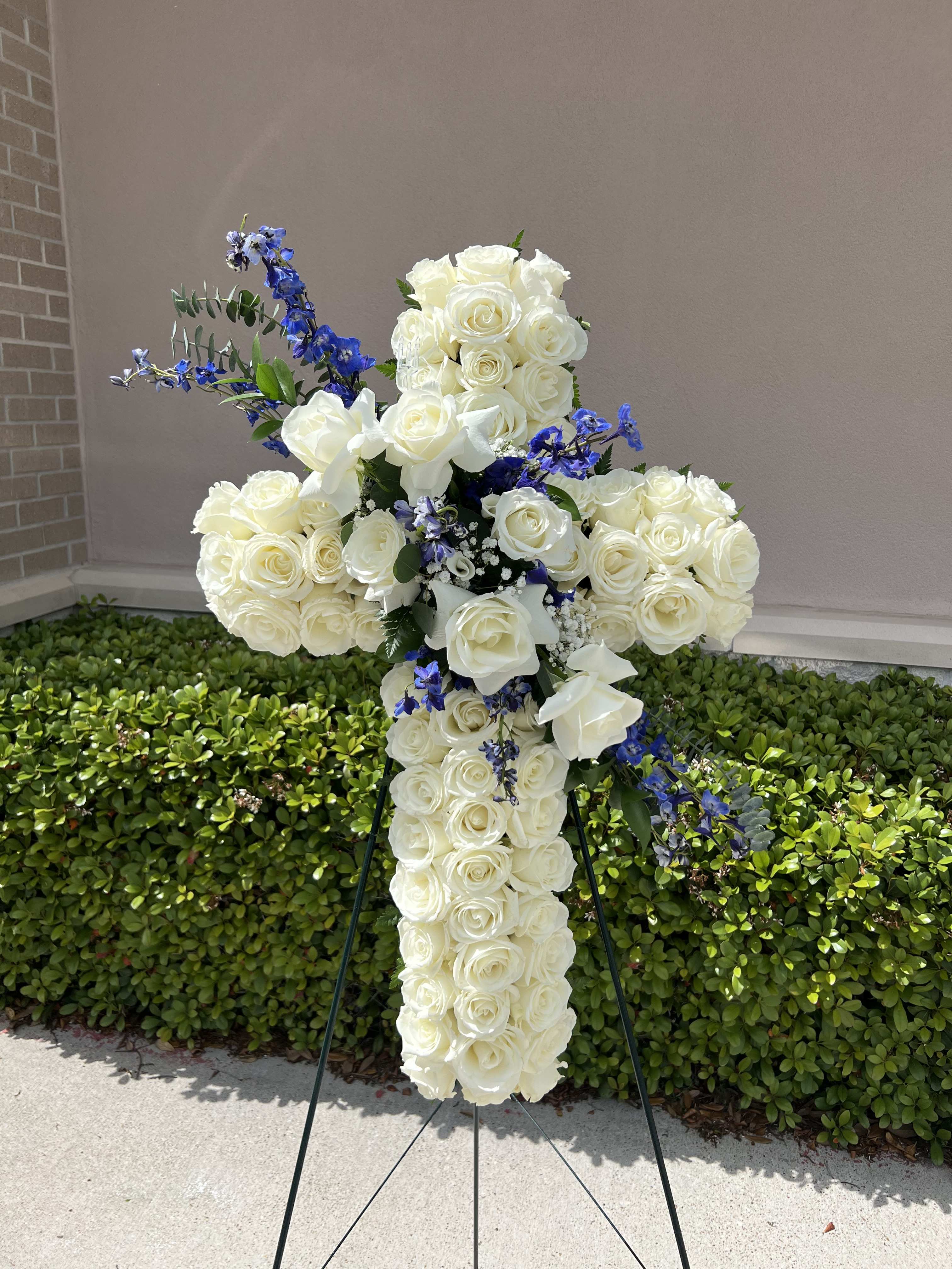 White rose cross-shaped floral tribute with blue accents on an easel