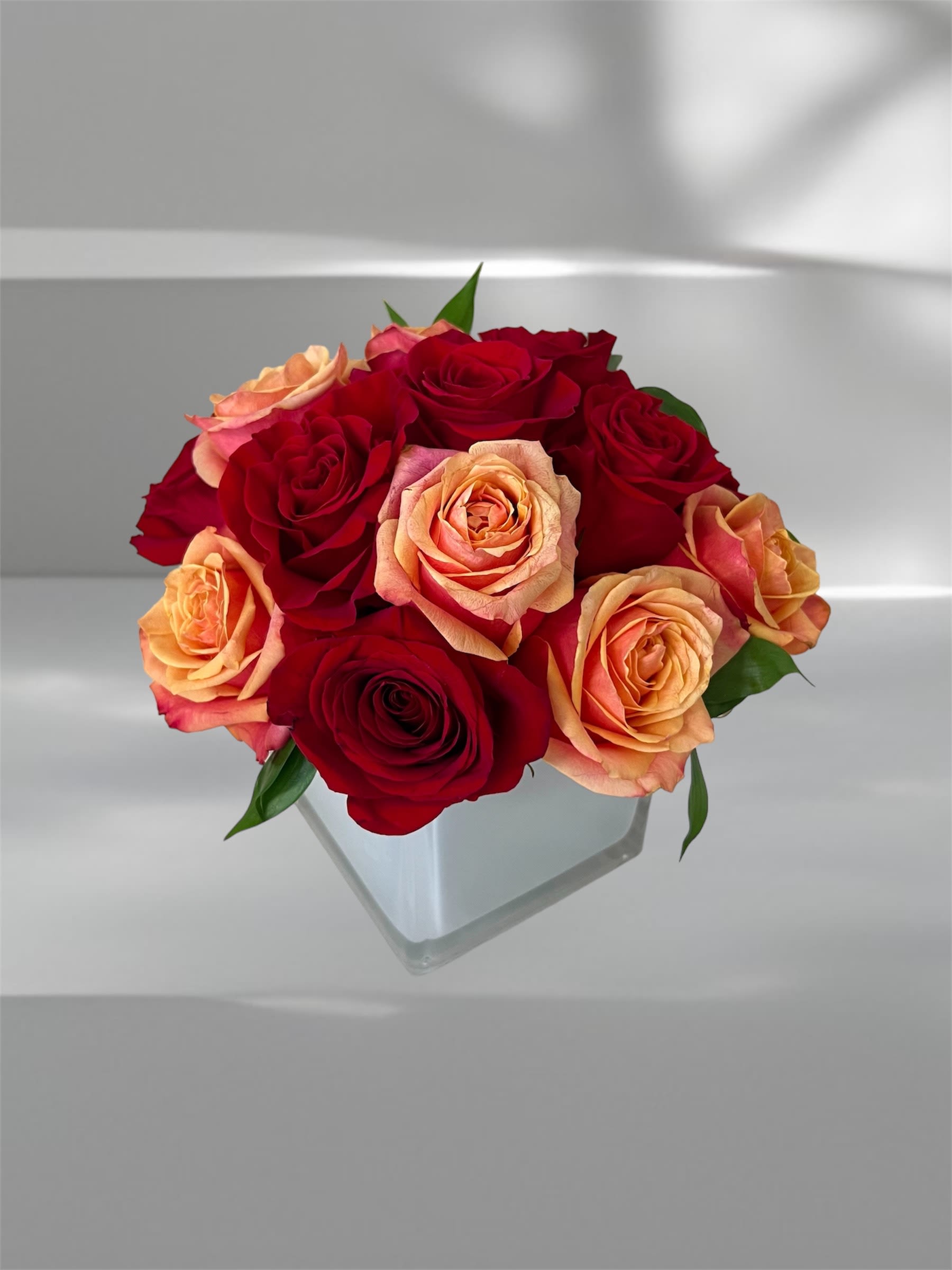 Red and peach roses arranged in a clear square vase