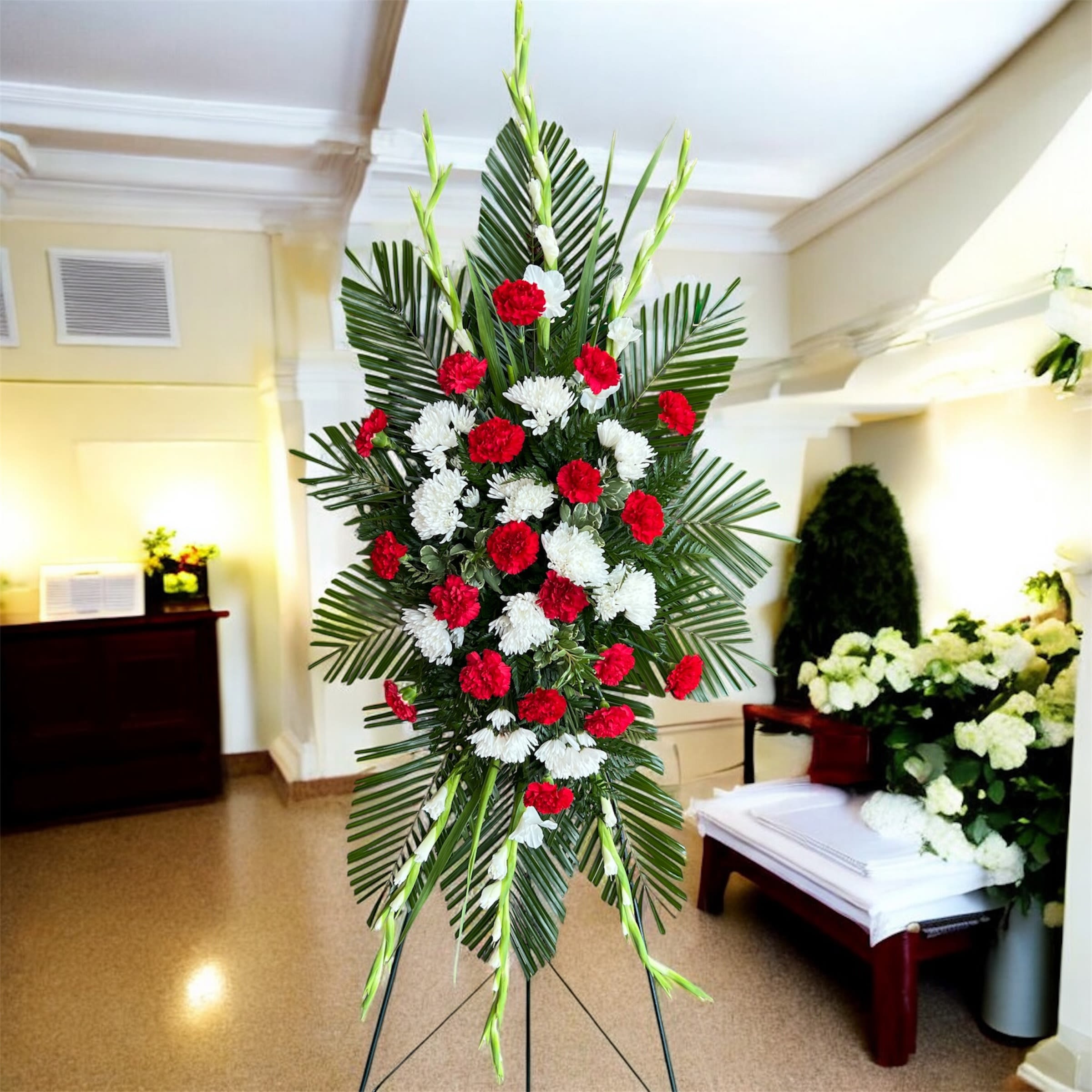 Standing floral spray with red and white carnations on a palm backdrop