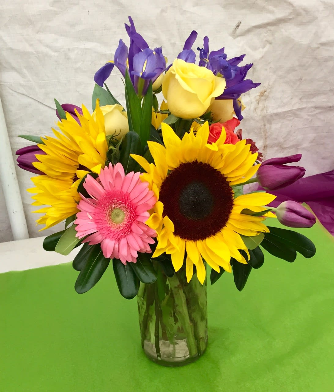 Colorful bouquet with sunflowers, roses, irises, and a gerbera daisy in a glass vase