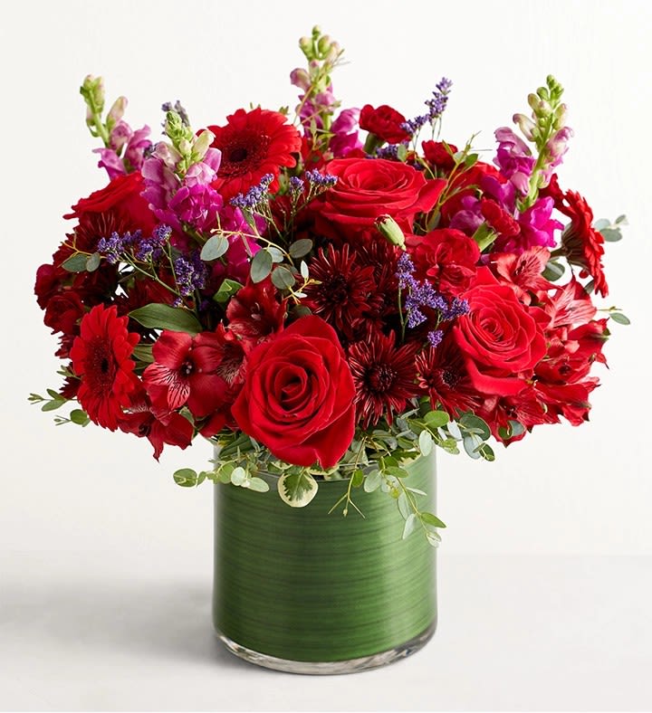 Red roses and mixed red flowers in a green glass vase