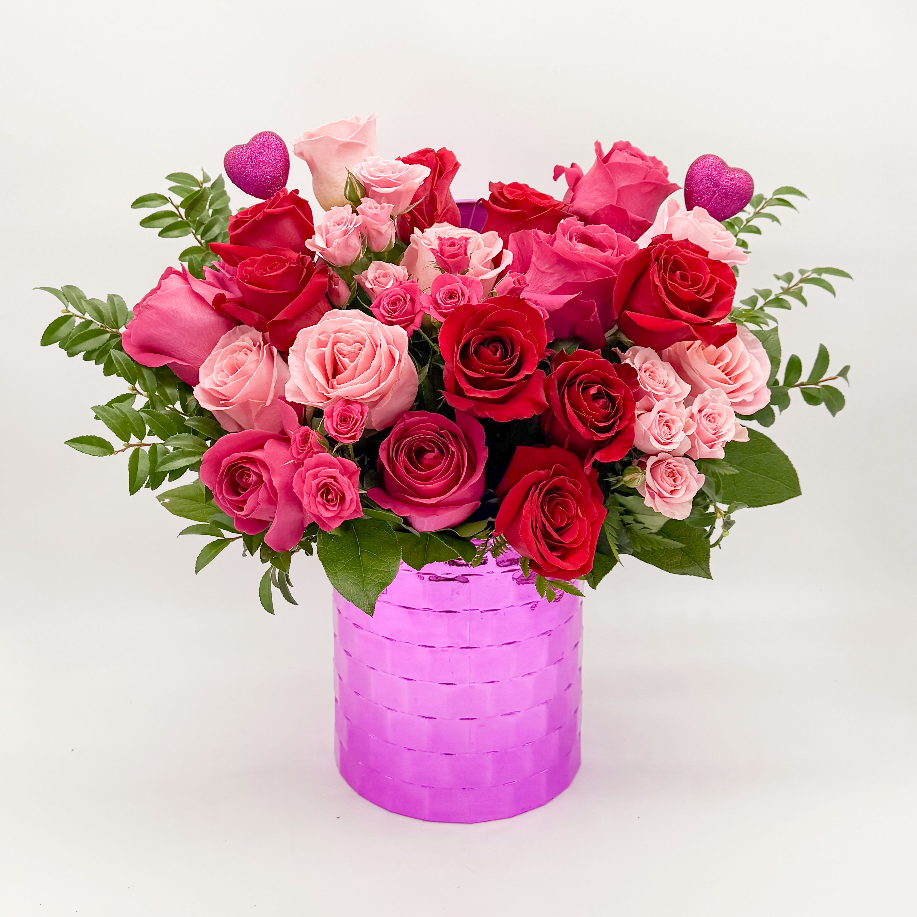 Pink and red roses in a bright pink vase with glitter heart picks