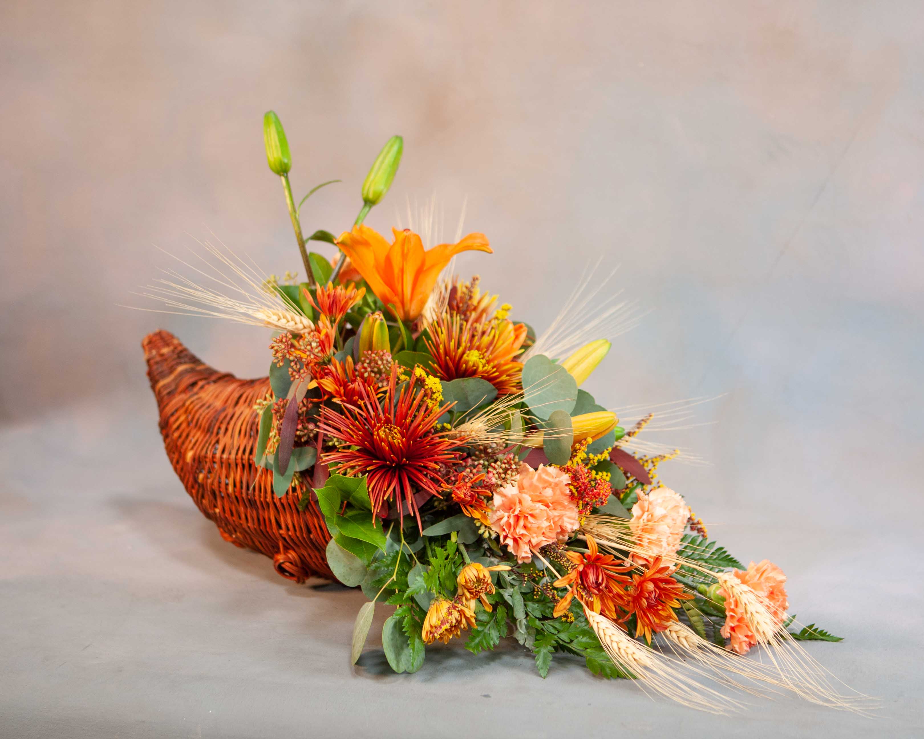 Orange floral arrangement in a woven basket with lilies and mums